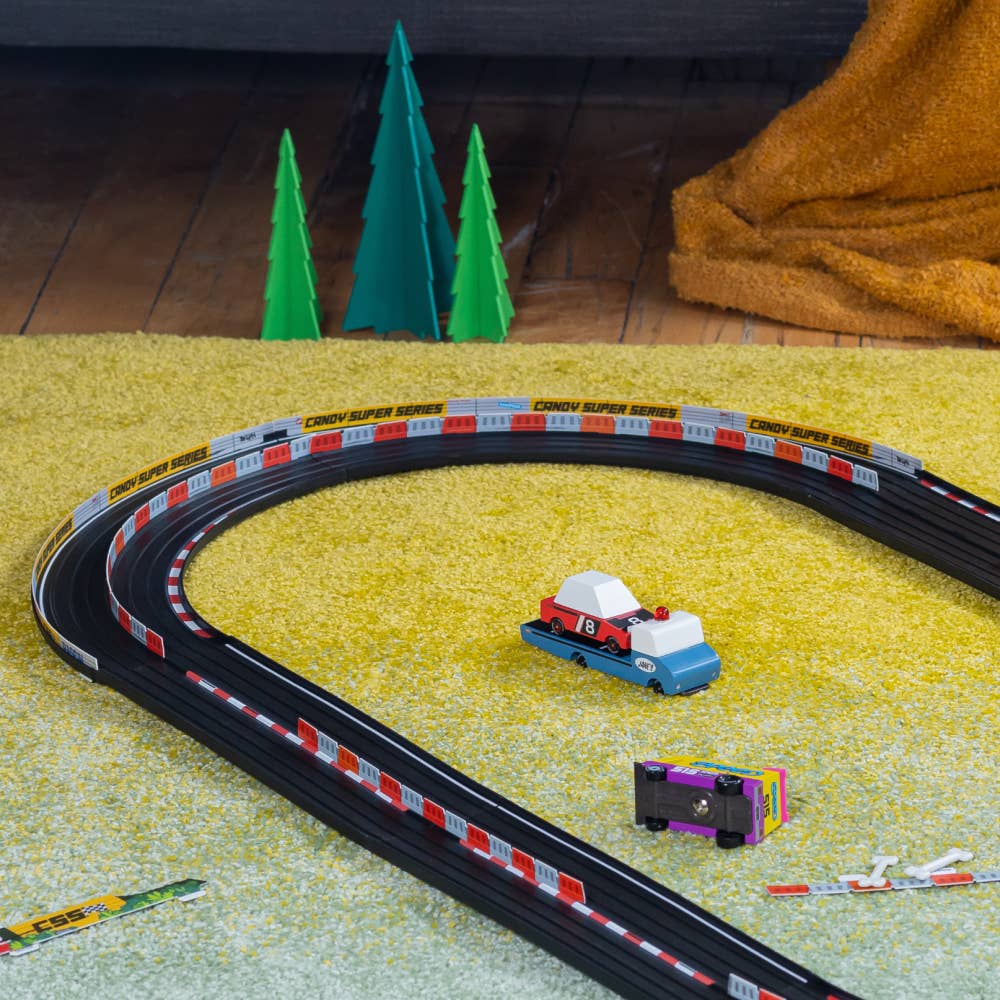 Toy car track set on a carpeted floor with toy cars and trees in the background.