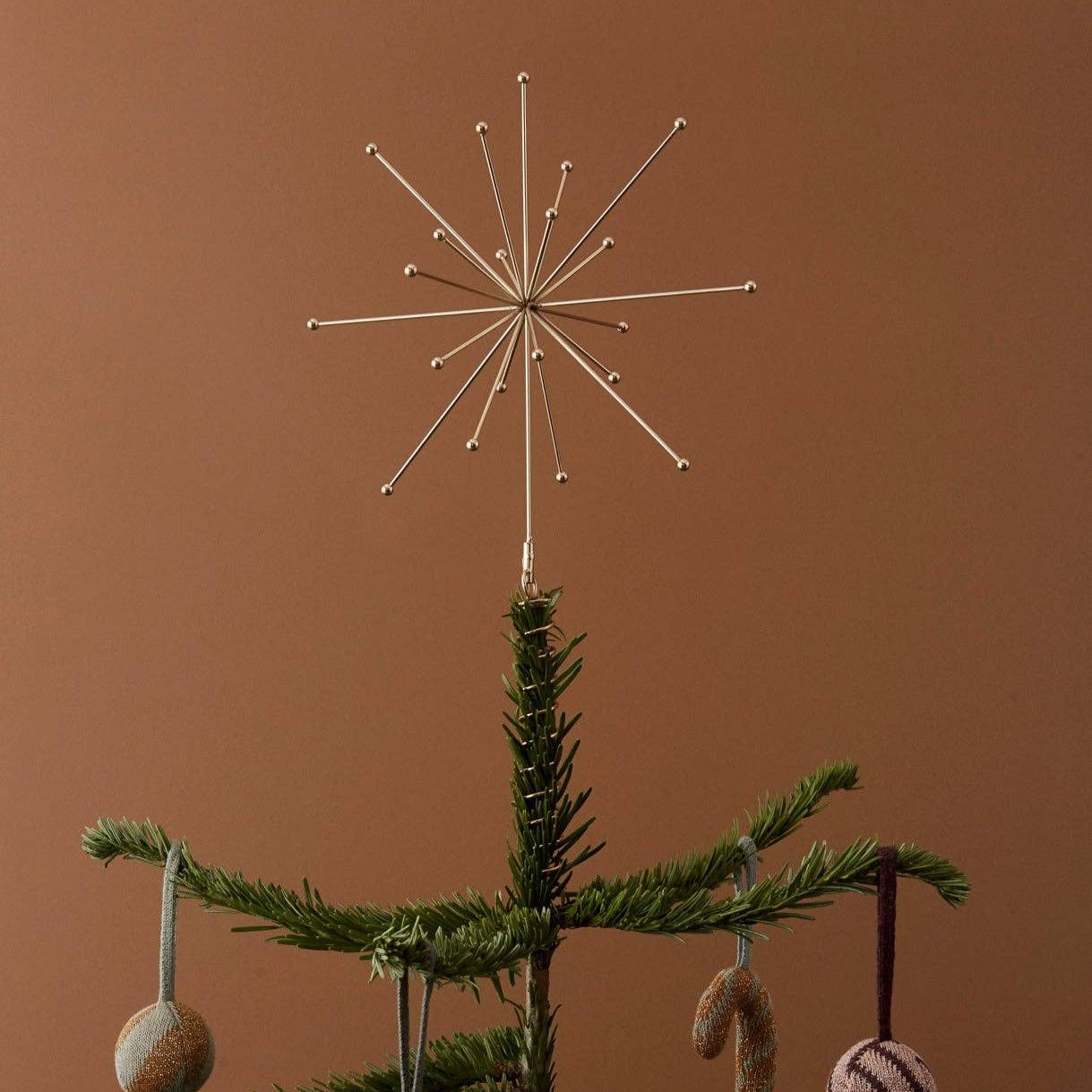 Decorative Christmas tree with a star-shaped topper and hanging ornaments against a brown background