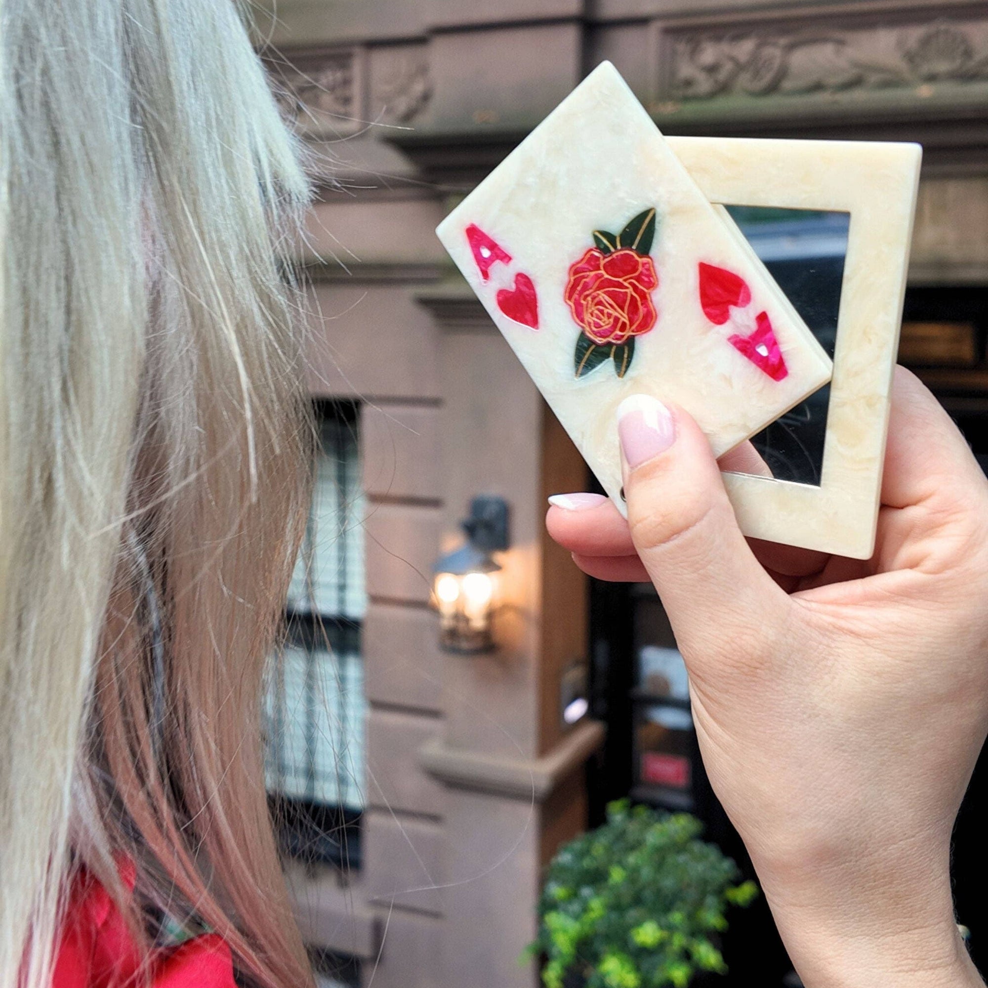 Person holding two playing cards with a rose design in an urban setting