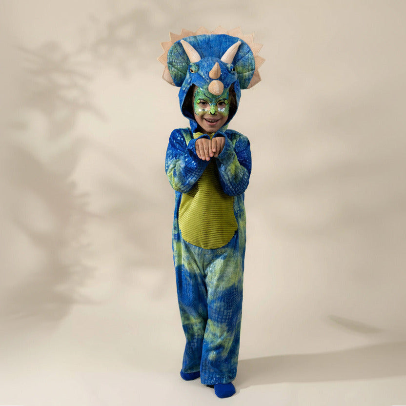 A child wearing a blue and green dinosaur costume with a hood featuring large horns and spikes, standing against a plain beige studio background.