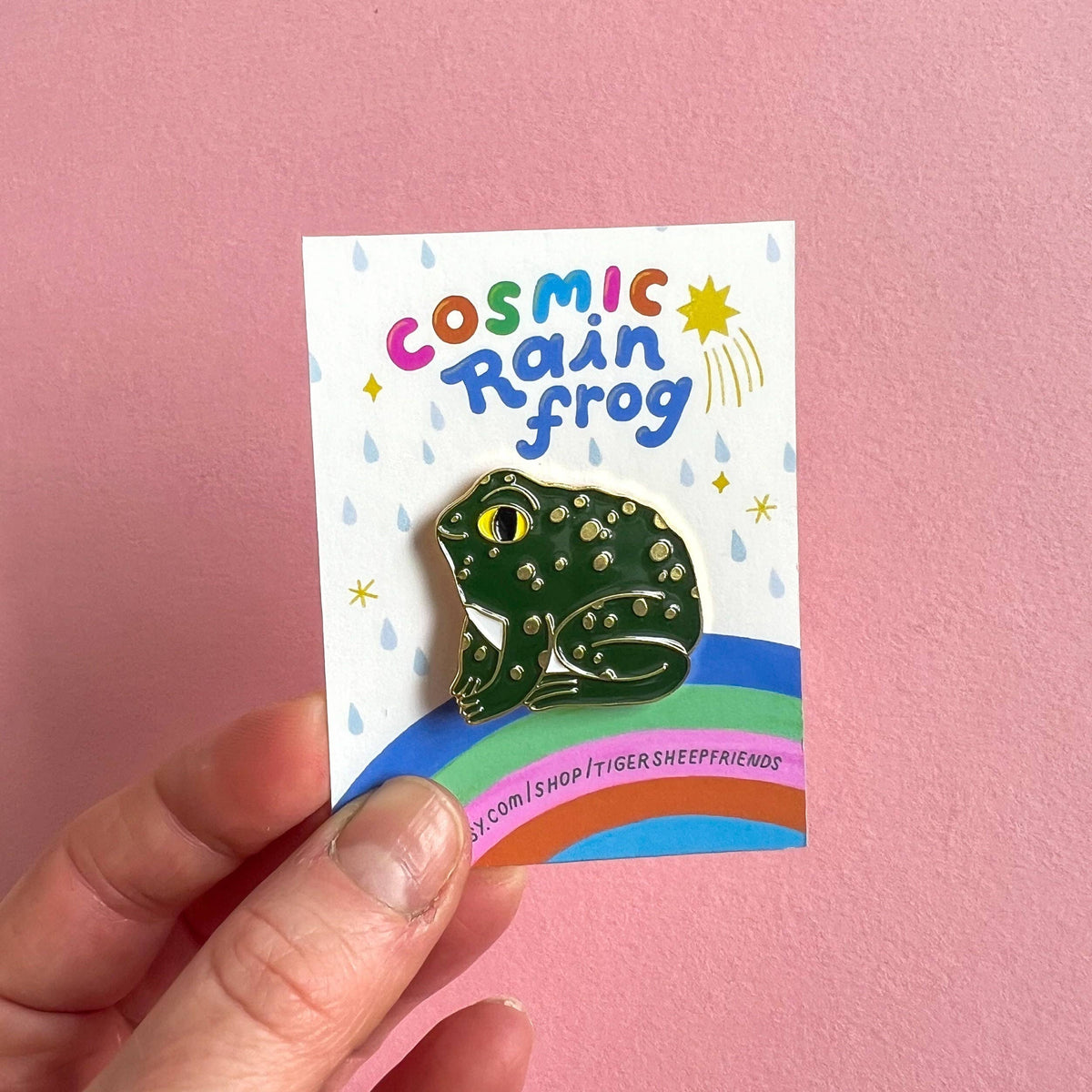 Frog-shaped pin on a card with 'Cosmic Rain frog' text against a pink background