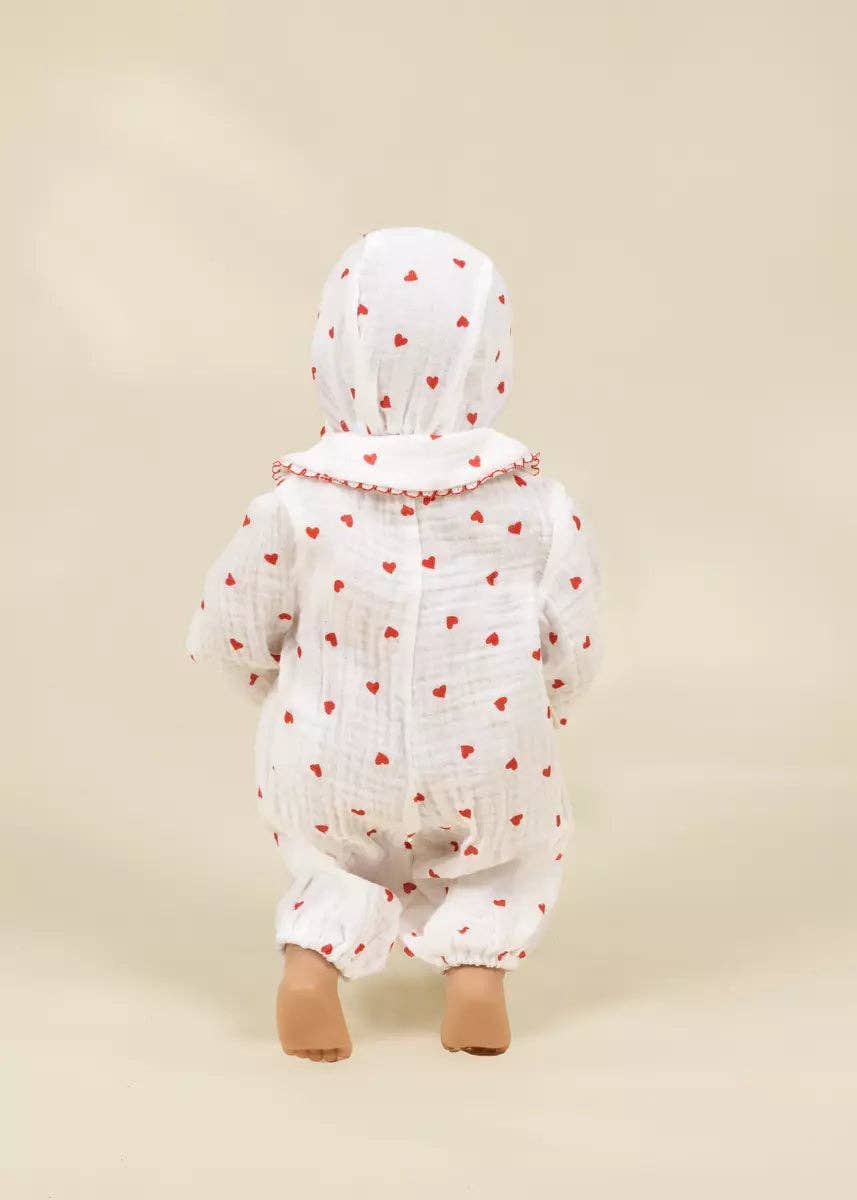 A baby wearing a white muslin hooded jumpsuit with a red heart pattern, shown from the back against a solid beige background.