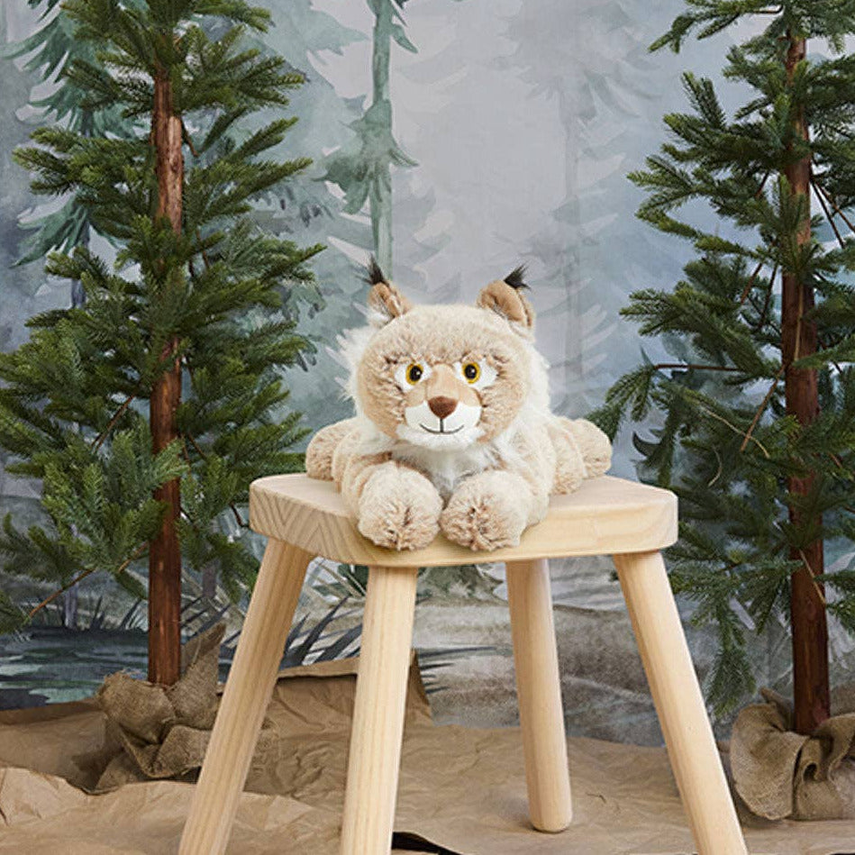 Plush lynx toy on a wooden stool with a forest background