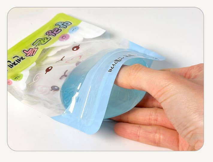 A hand holding a light blue translucent silicone pouch or pocket against a plain white background, with part of a printed backing card visible.