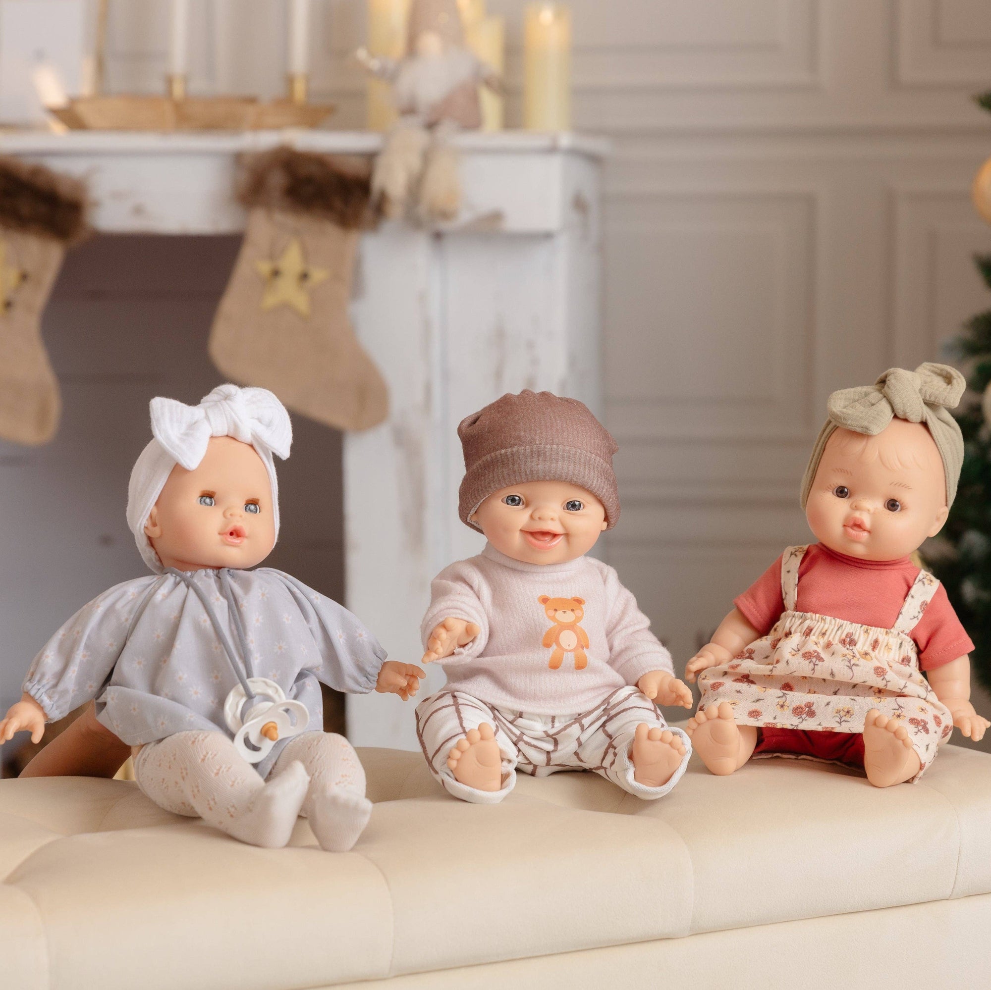 Three dolls sitting on a couch in a festive room with Christmas decorations.