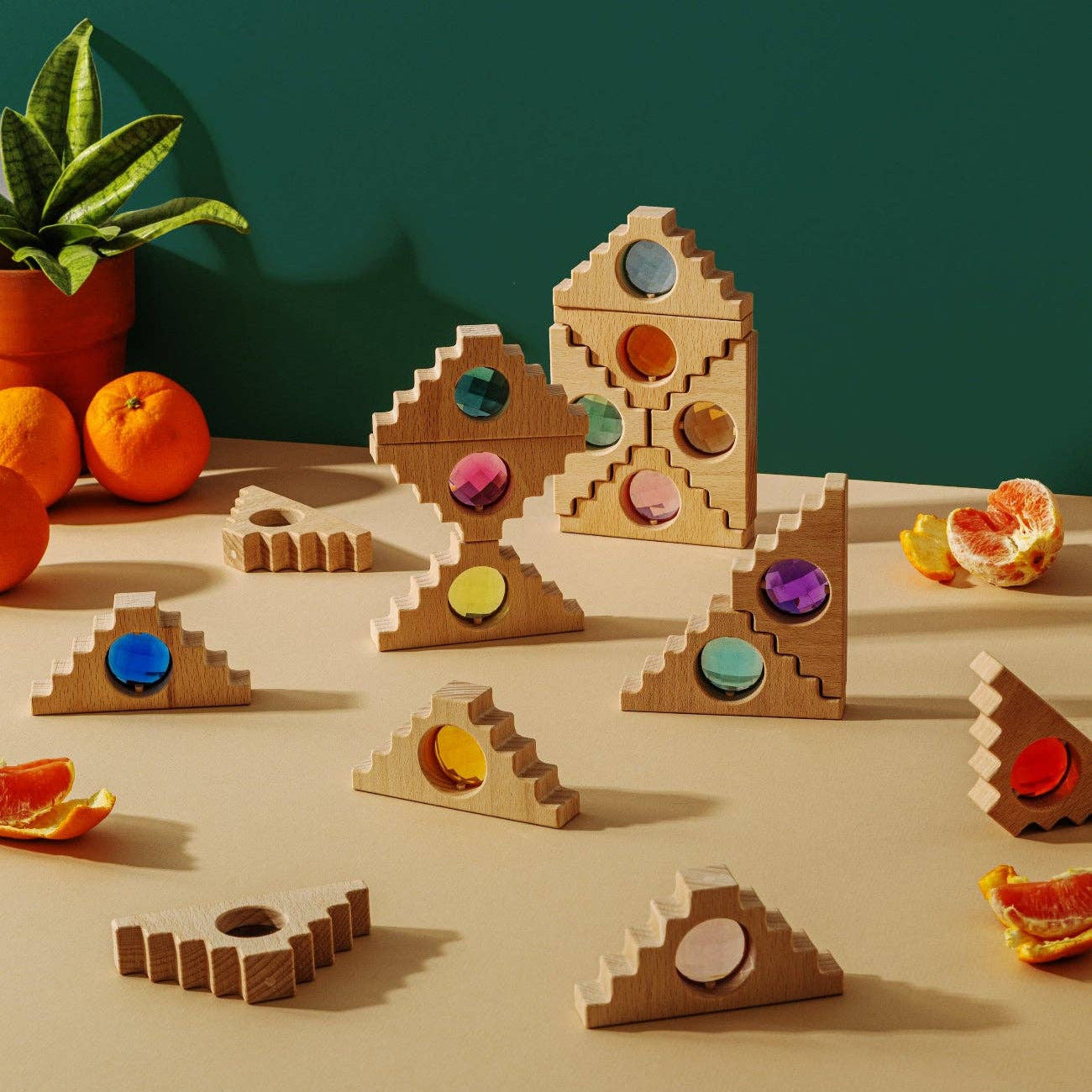 Wooden geometric shapes with colorful circular pieces on a beige surface with oranges and a plant in the background.