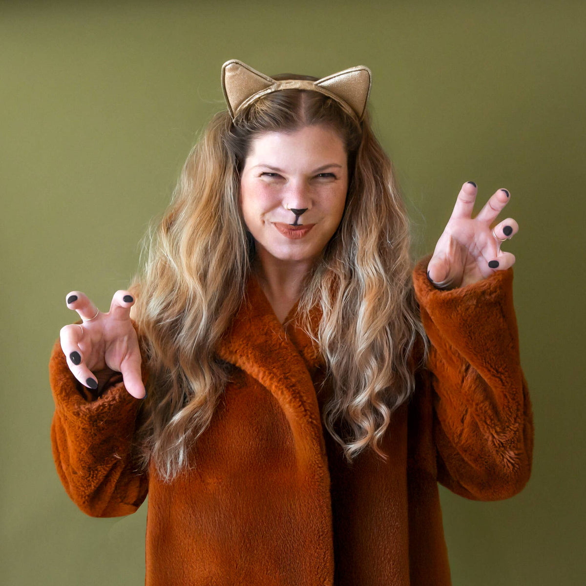 Person wearing a fox costume with ears and face paint against a green background