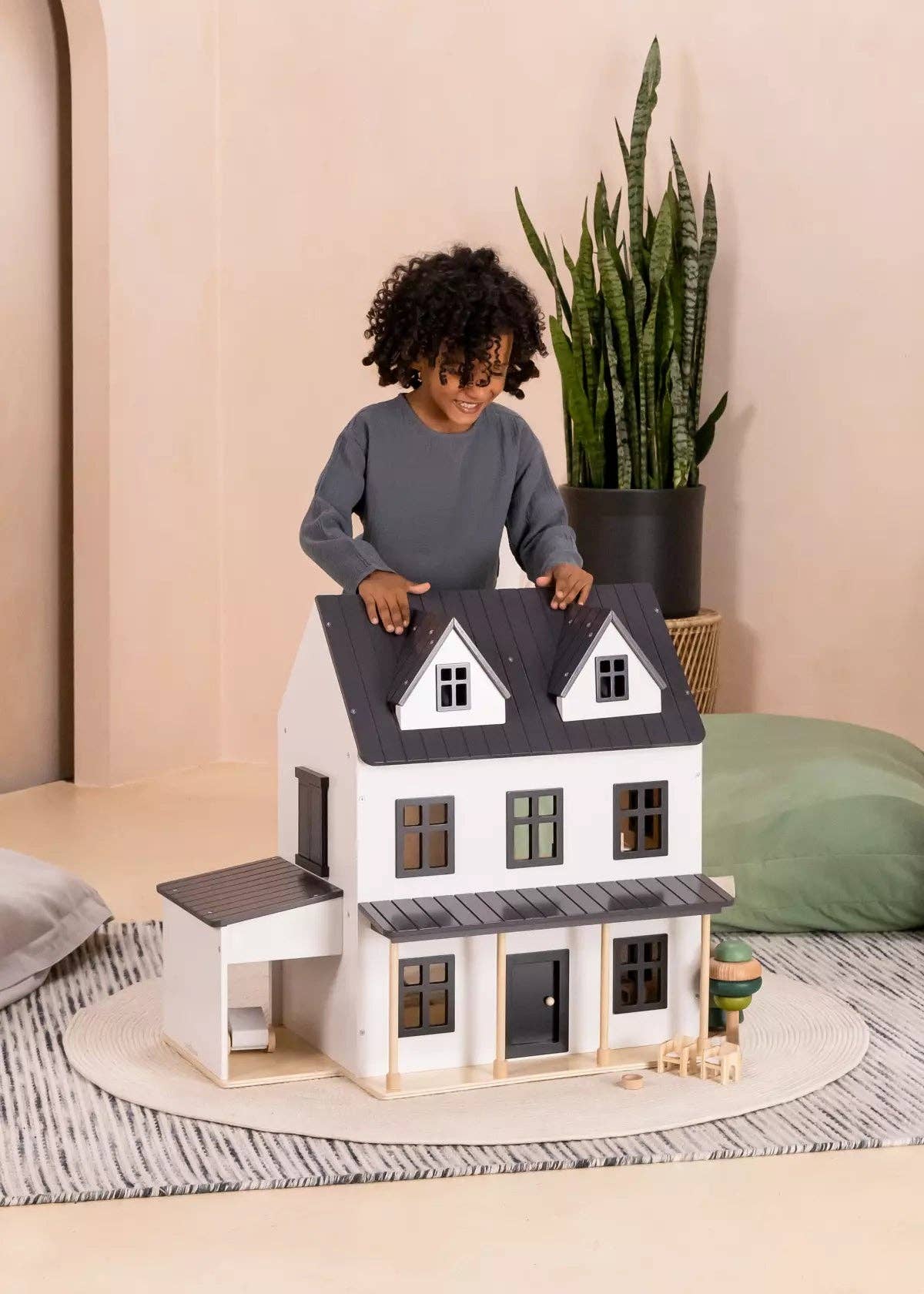 Child playing with a toy house on a bed with a plant in the background