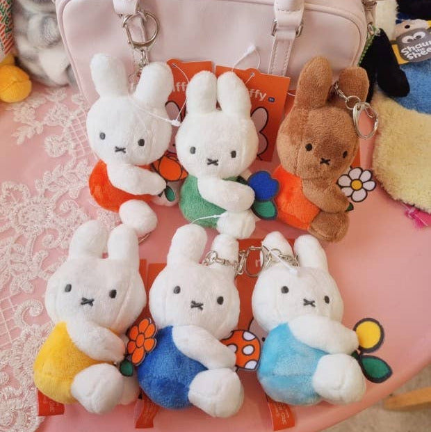 Set of plush rabbit keychains on a pink surface with a white bag in the background.