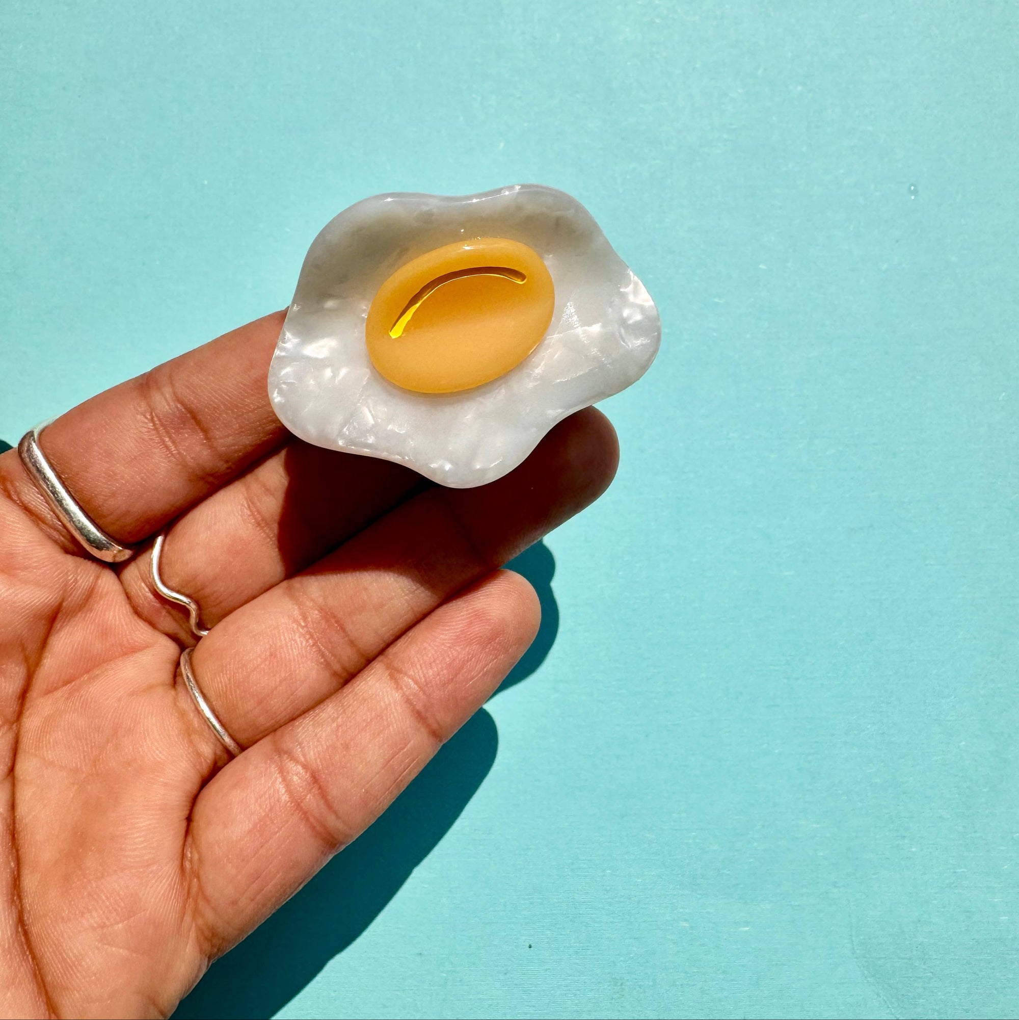 Hand holding a small toy egg 
 against a light blue background