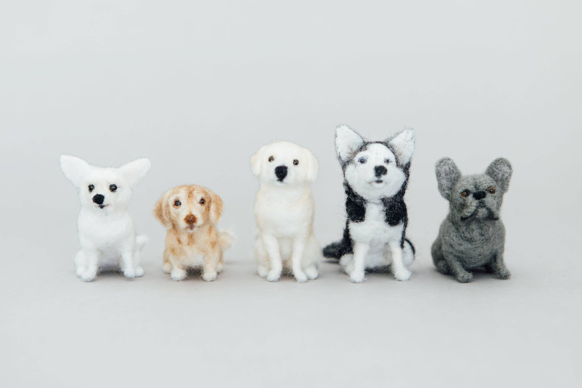 Five small dog figurines in different breeds, including white, tan, black and white, and gray, lined up against a light gray background.