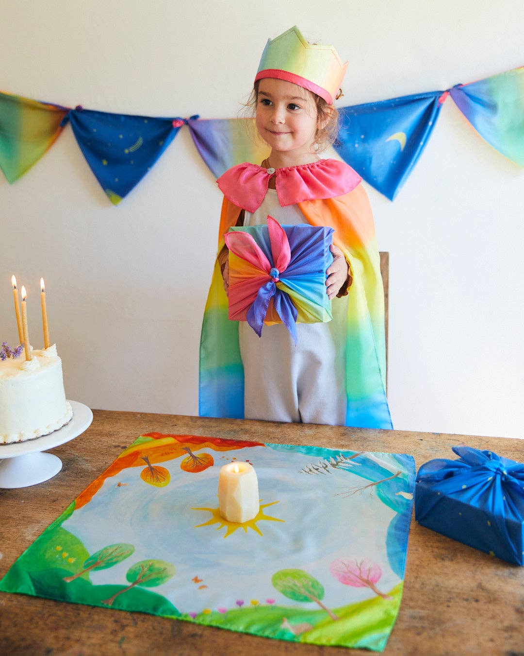 Child in a rainbow-themed costume with birthday cake and decorations
