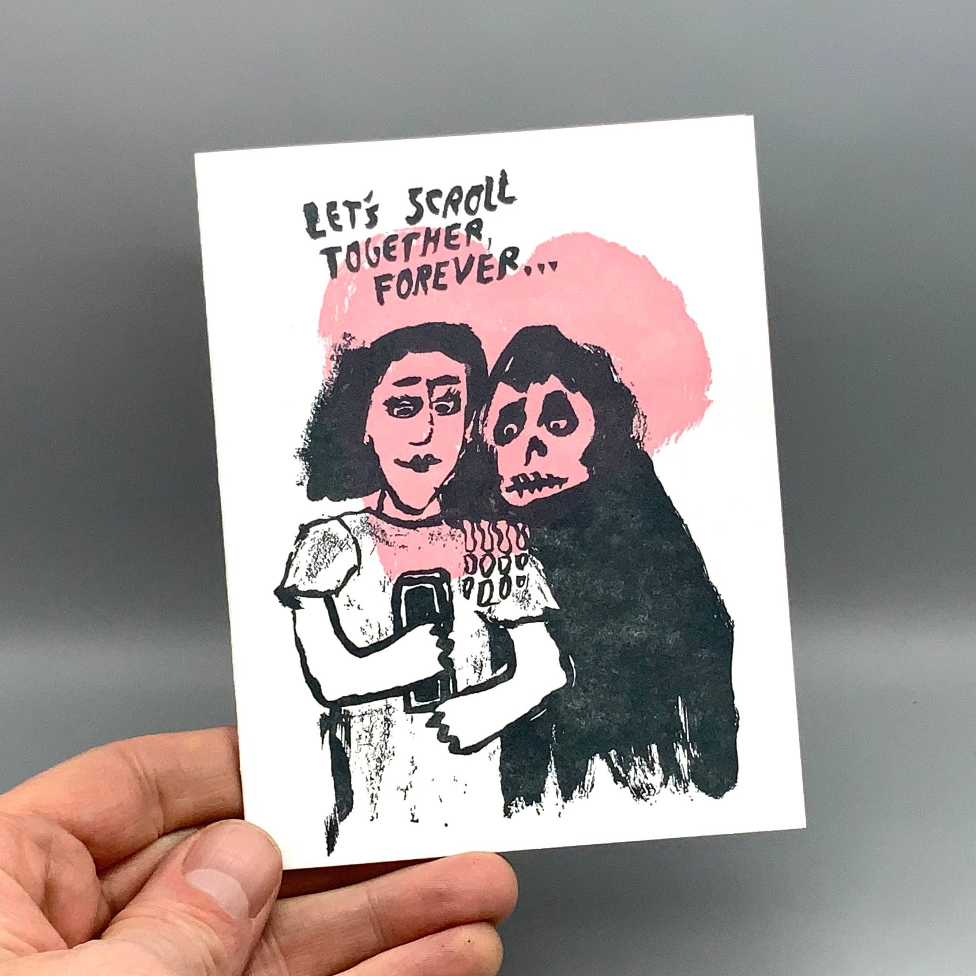 Hand holding a card with illustration of two people hugging and text 'Let's scroll together forever' on a gray background