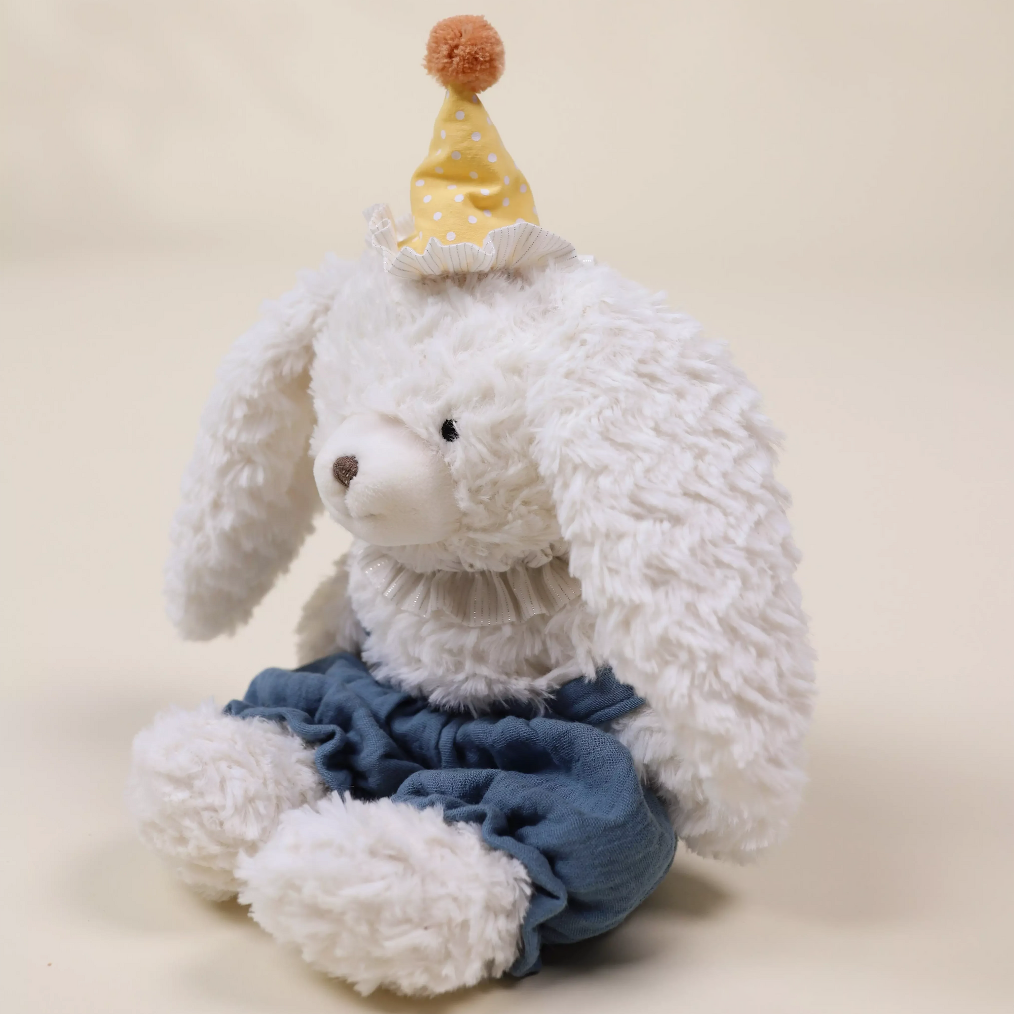 White plush toy with  blue overalls and yellow hat on a beige background