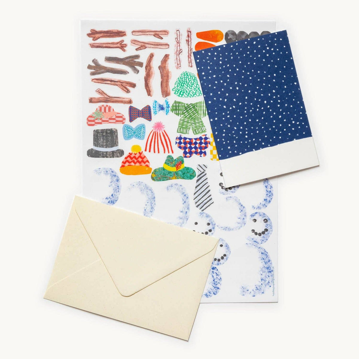 A sheet of illustrated stickers or decoupage papers with whimsical drawings, shown with a cream envelope on a white background. The sheet includes colorful clothing, accessories, and abstract blue scribbled motifs, with one folded corner revealing a navy blue patterned backing.