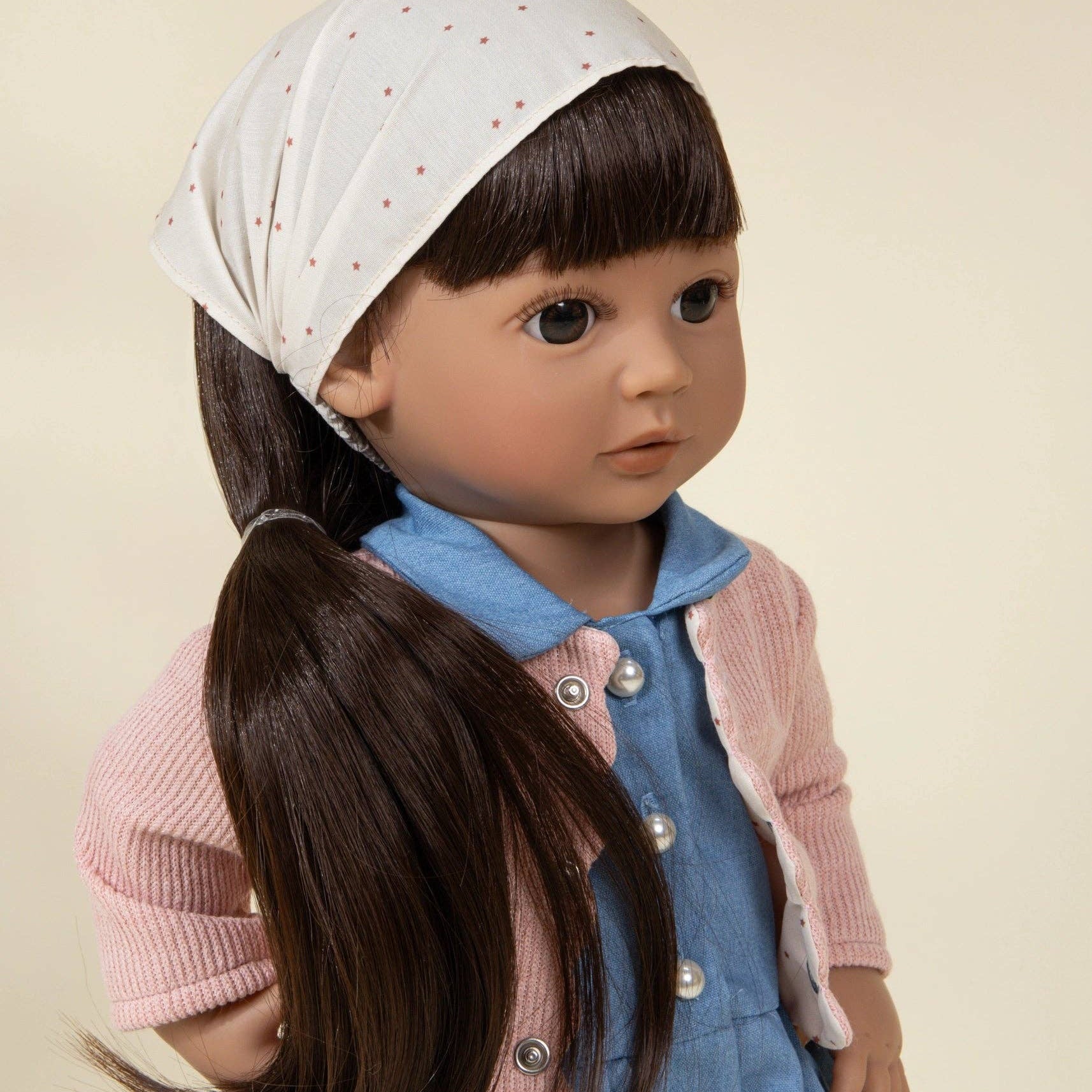 Doll wearing a pink cardigan, blue dress, and white headscarf on a beige background