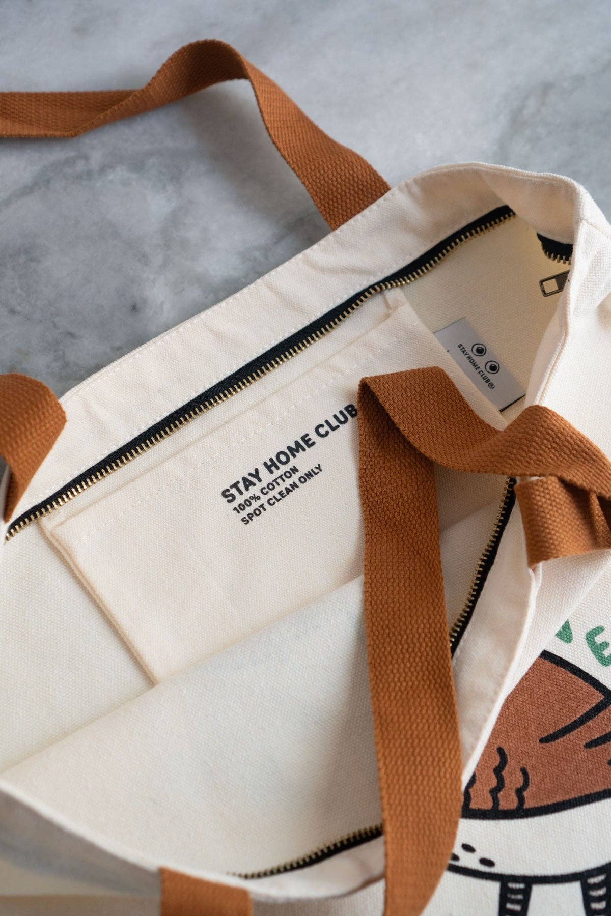 White tote bag with brown handles and a cat illustration on a gray surface