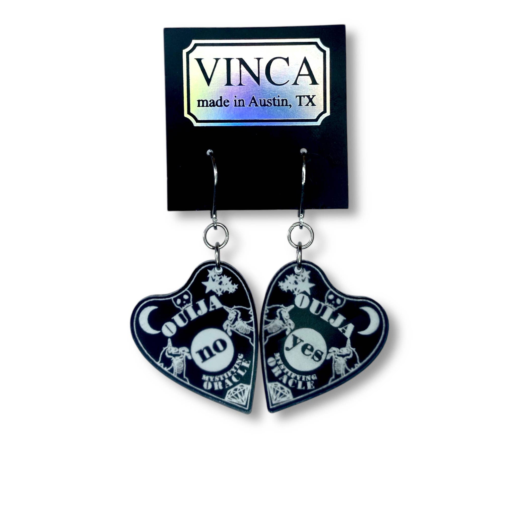 Heart-shaped earrings with 'Ouija' design on a black card with 'VINCA' branding.
