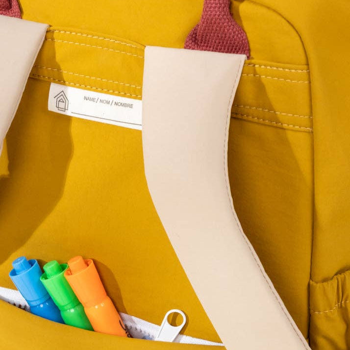 Yellow backpack with colorful markers in a pocket, featuring a visible brand label.