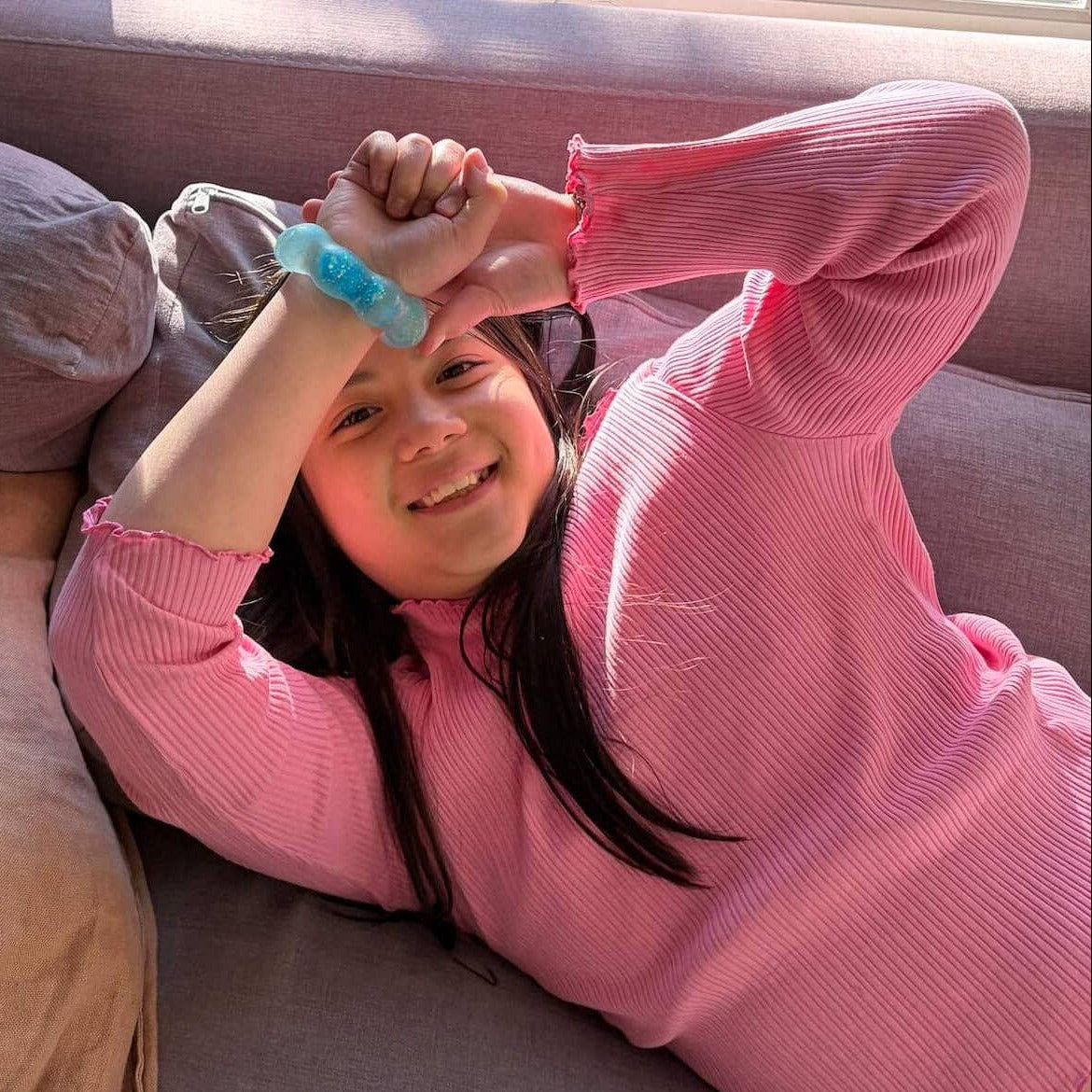 Child in a pink sweater lying on a couch with a blue bracelet