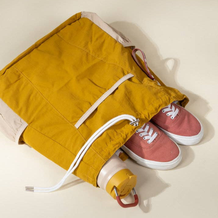 Yellow drawstring bag with pink sneakers inside on a light beige background