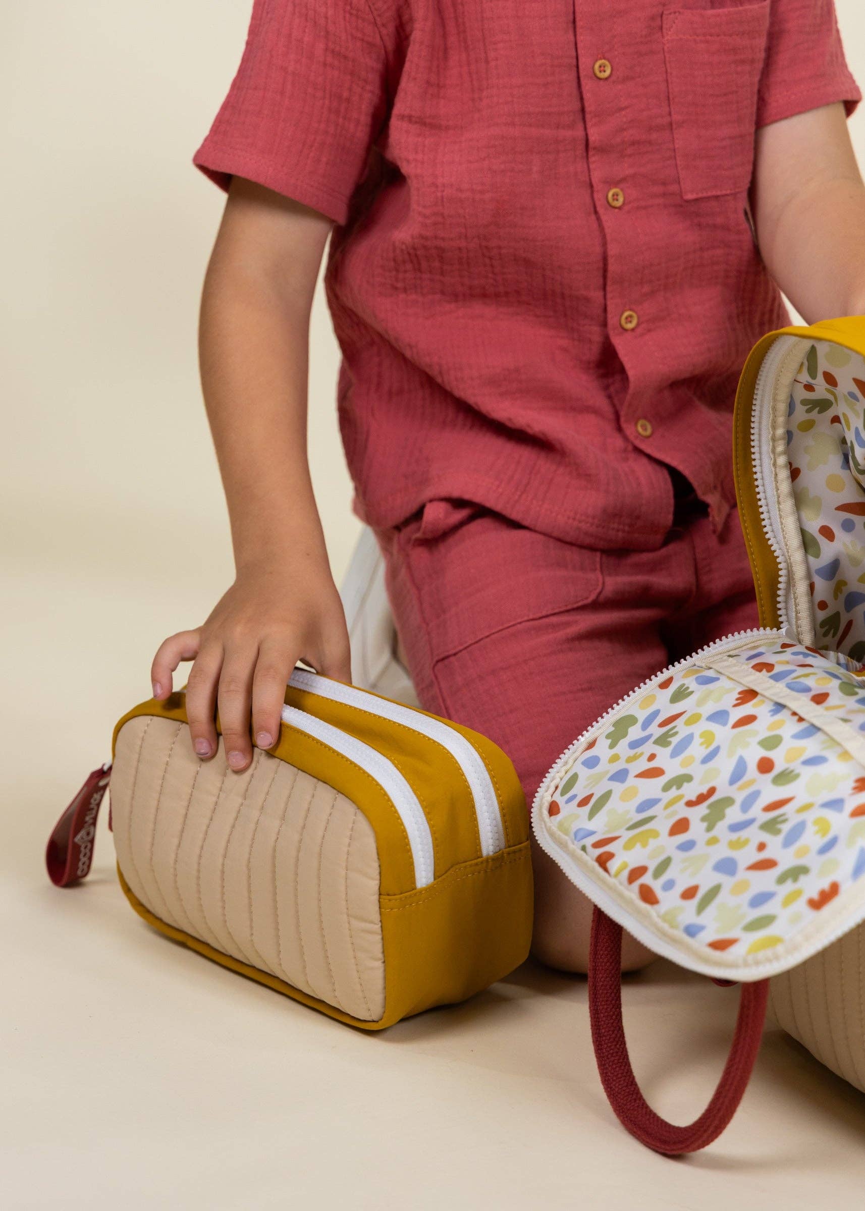 Person holding a textured pouch with another colorful bag on a neutral background