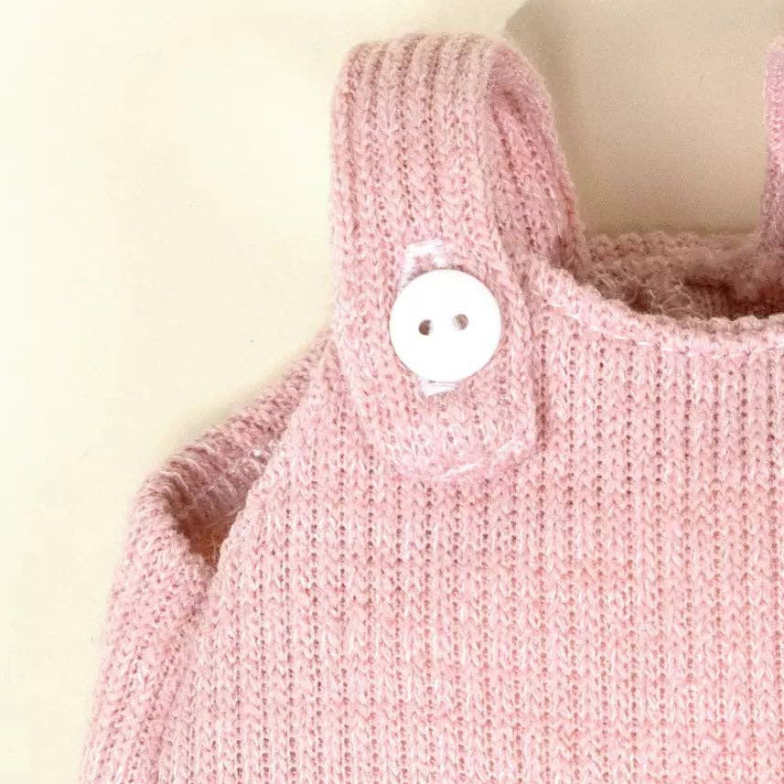 Pink knitted baby romper with a button on a beige background