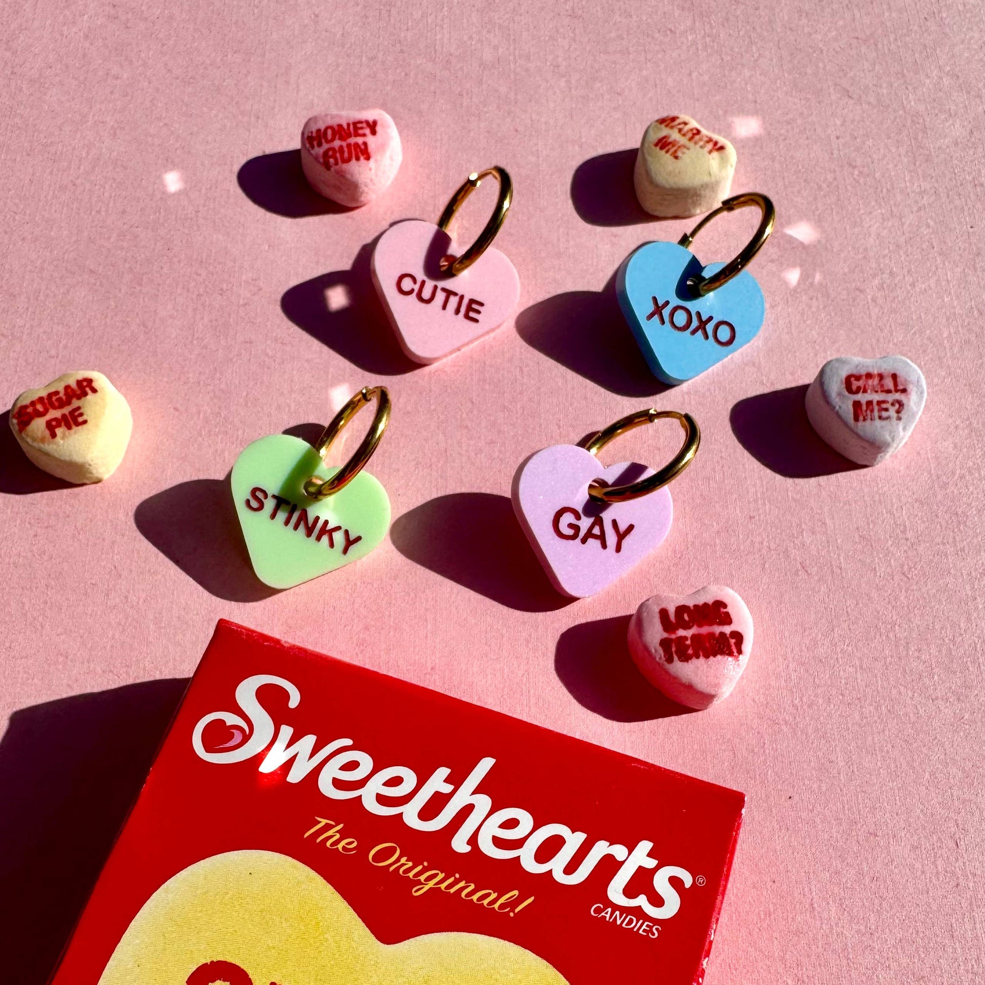 Sweethearts candy hearts with various messages on a pink background, featuring the Sweethearts packaging.