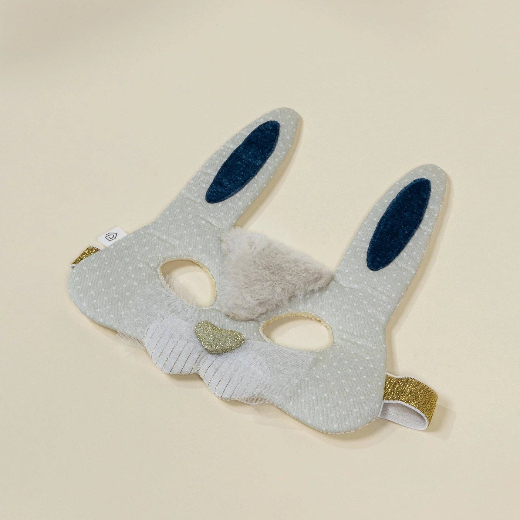 Gray bunny mask with black eyes and green accents on a beige background