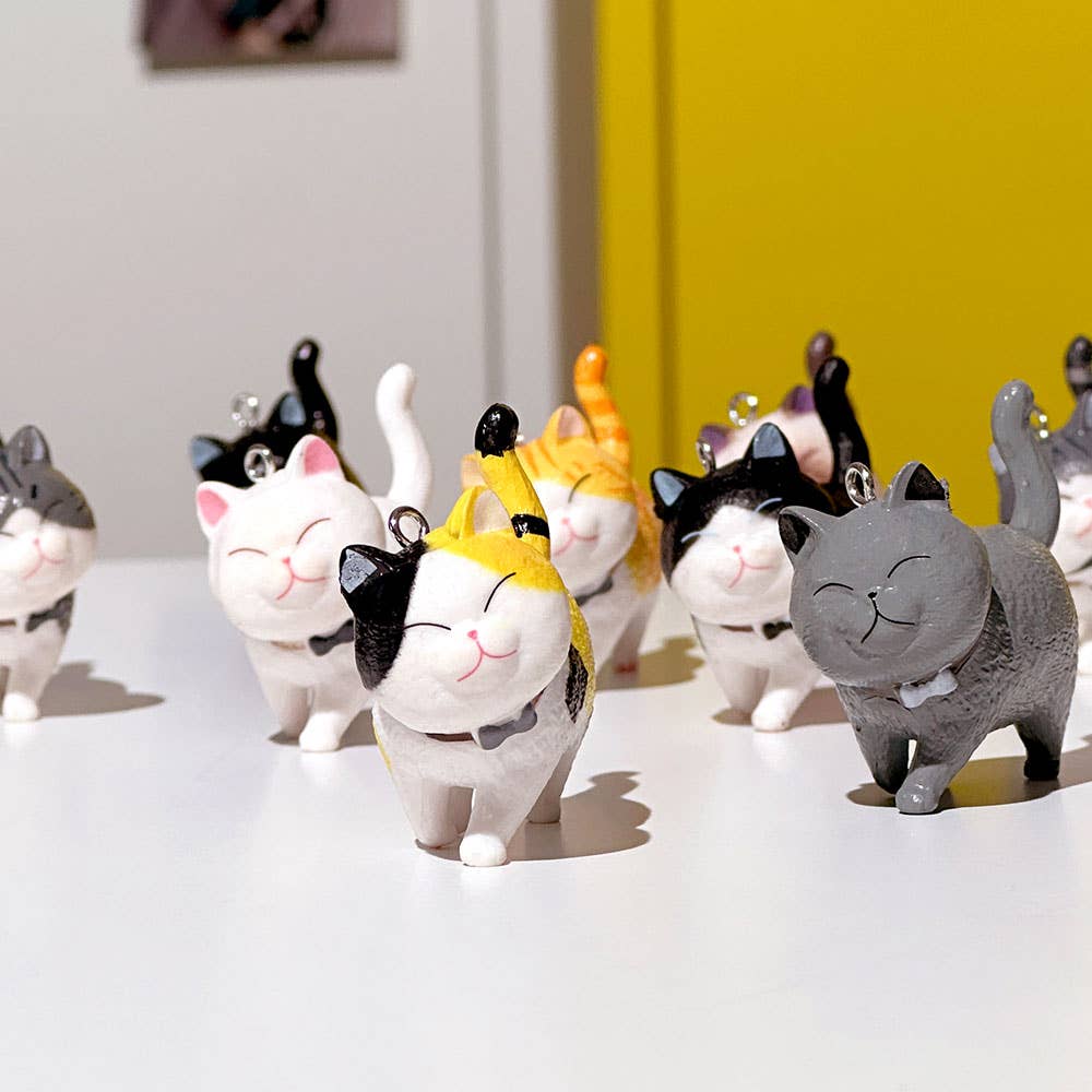 Collection of cat-shaped figurines on a white surface with a yellow wall in the background.