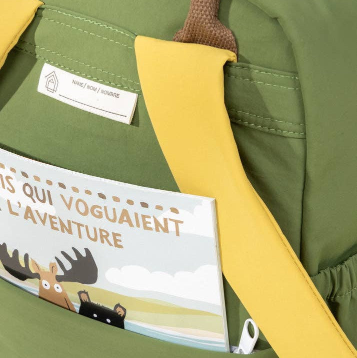 Green backpack with a yellow strap featuring a children's book titled 'L'Aventure'.