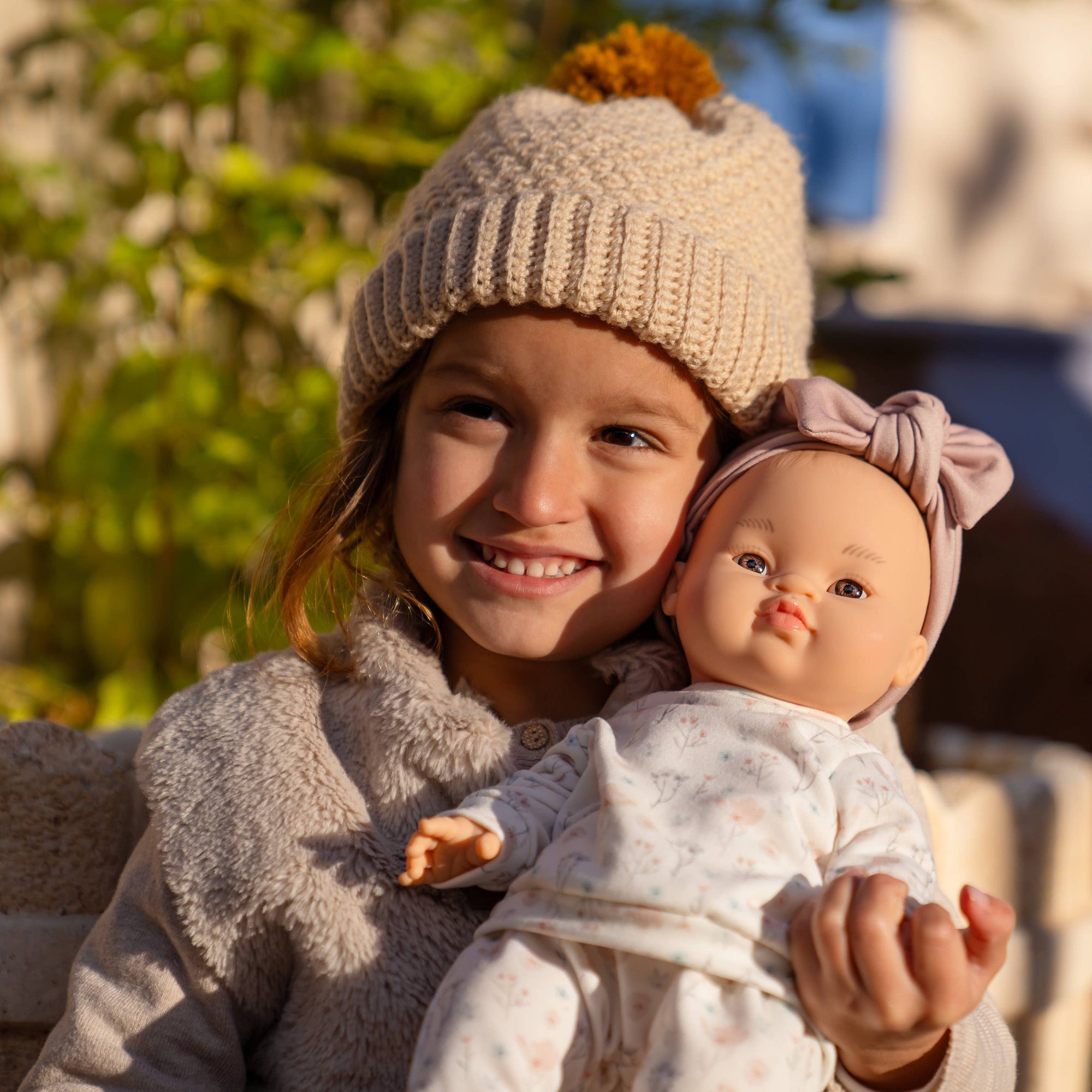 Child holding a doll outdoors on a sunny day
