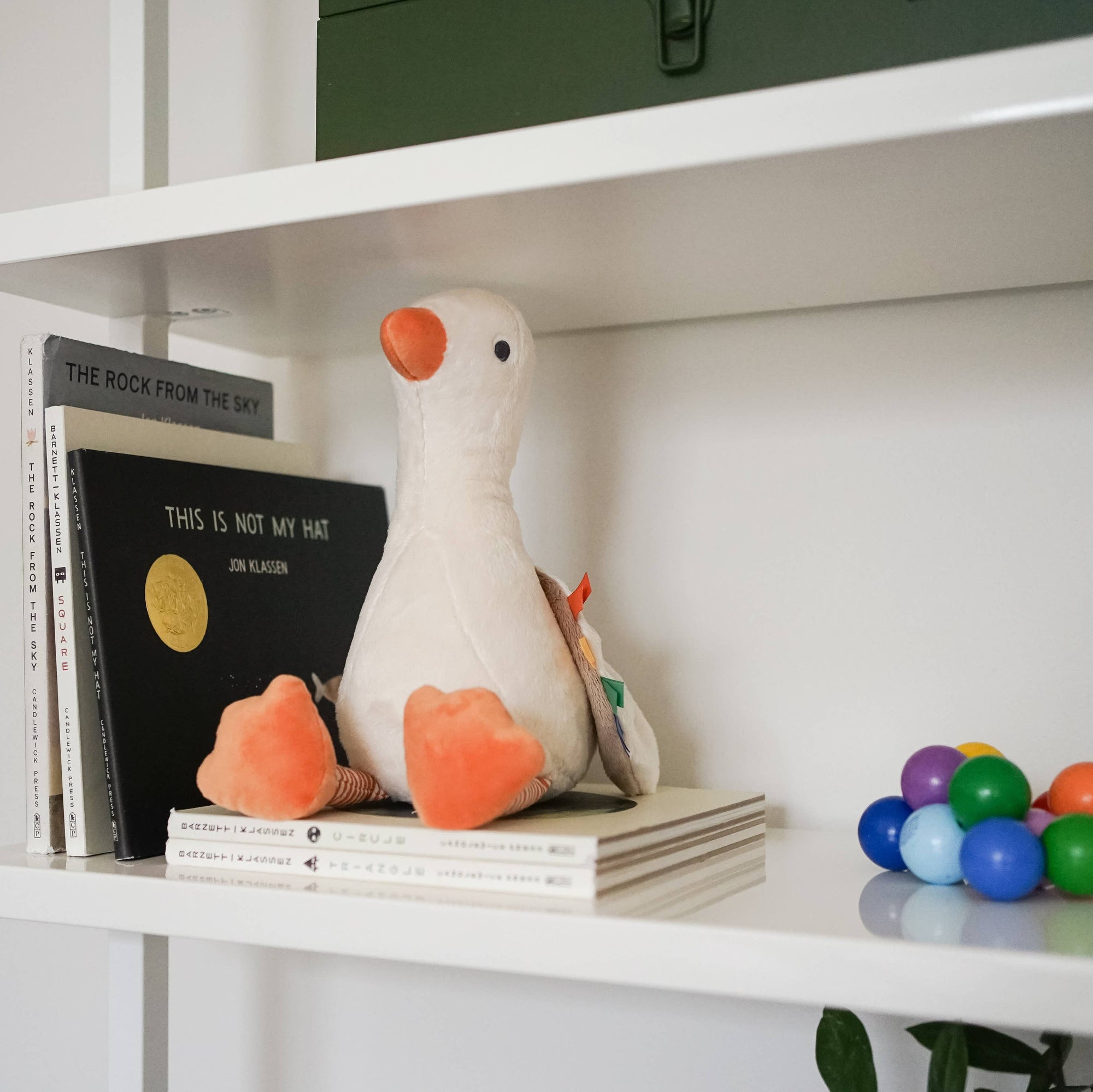 Plush toy duck on a shelf with books and colorful balls