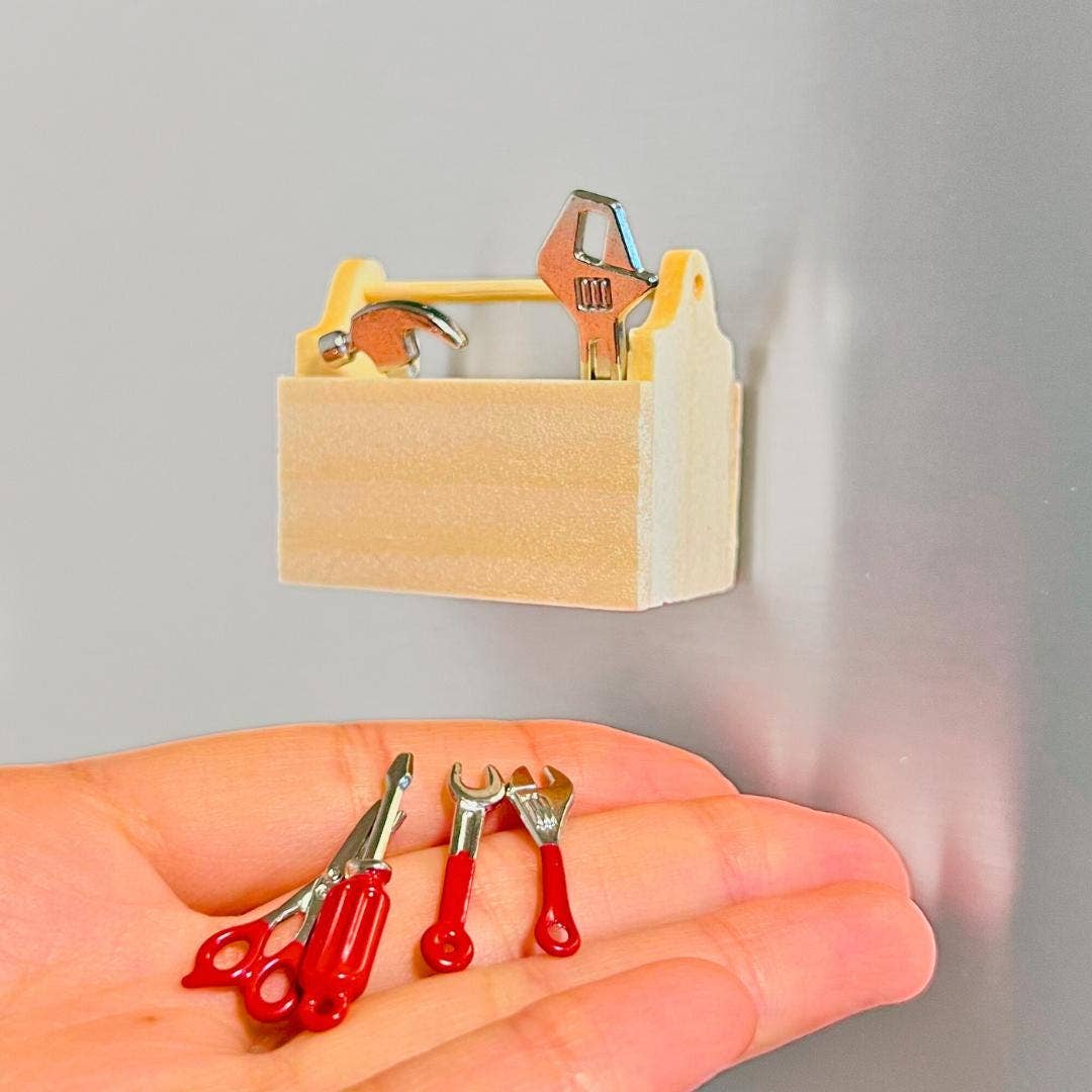 Miniature tools including a screwdriver, wrenches, and pliers in a wooden toolbox on a gray background.