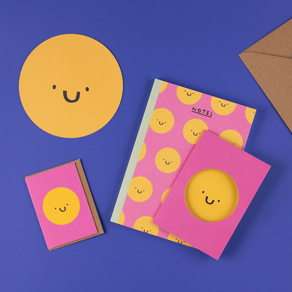 Notebooks with yellow smiley face design on pink covers, placed on a blue background.