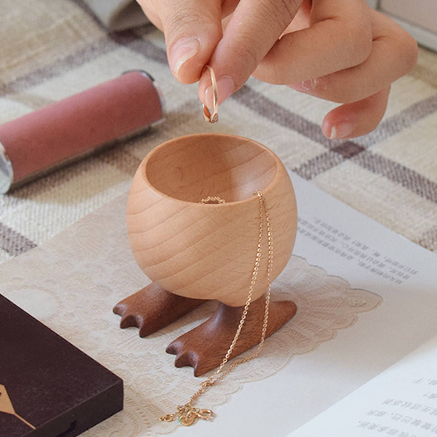 Wooden jewelry holder with a hand placing a necklace inside, on a checkered fabric background.
