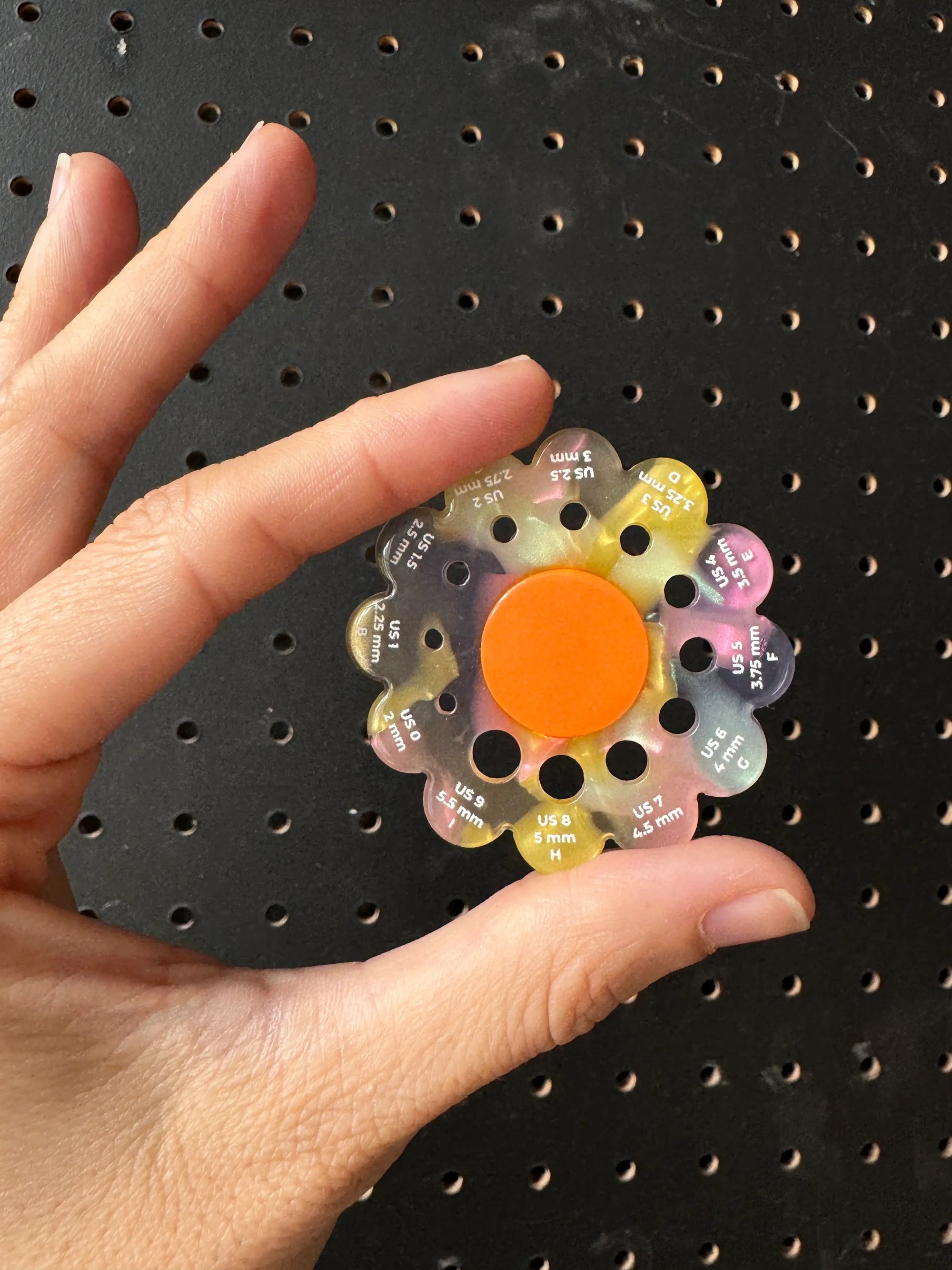 Colorful wheel with numbers held by a hand against a black pegboard background