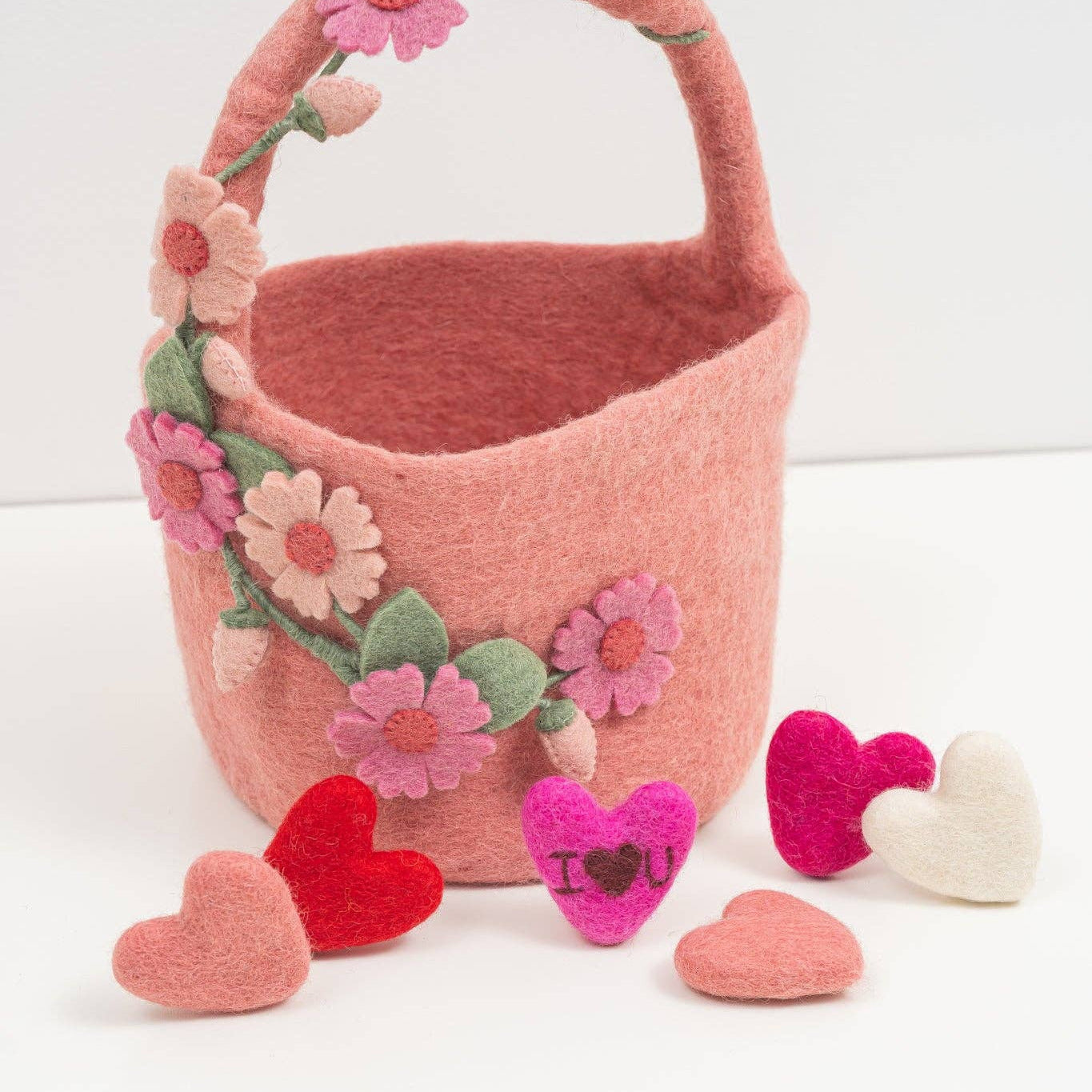 Pink felt basket with floral decorations and heart-shaped accessories on a white background