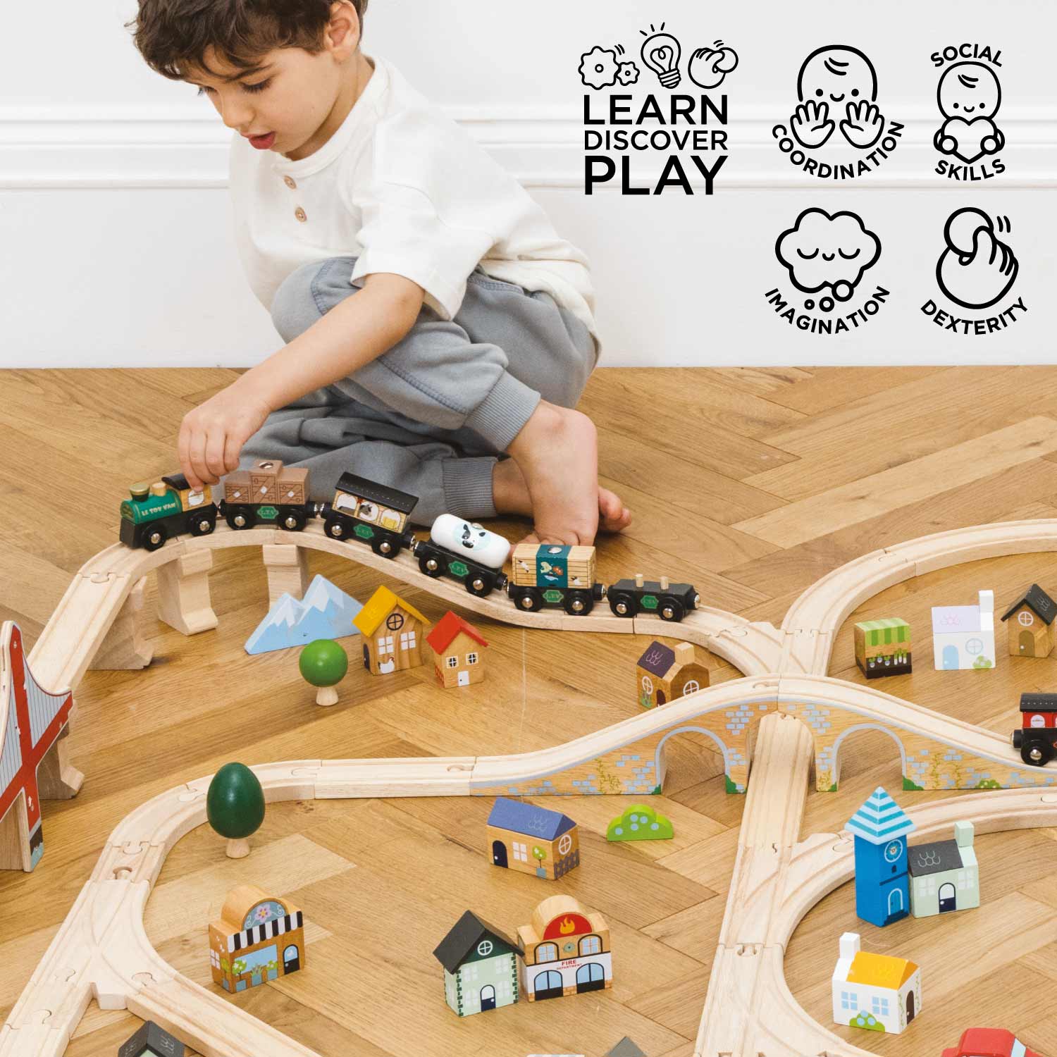 Child playing with a wooden train set on a wooden floor, with educational icons above.
