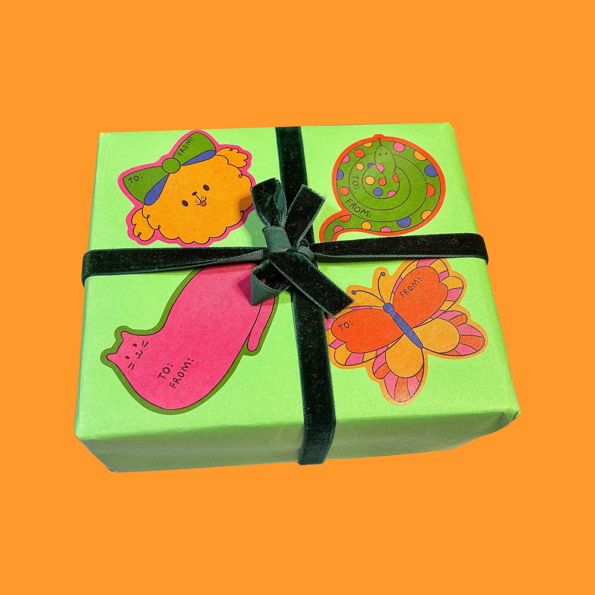 Green gift box with colorful stickers and a black ribbon on an orange background