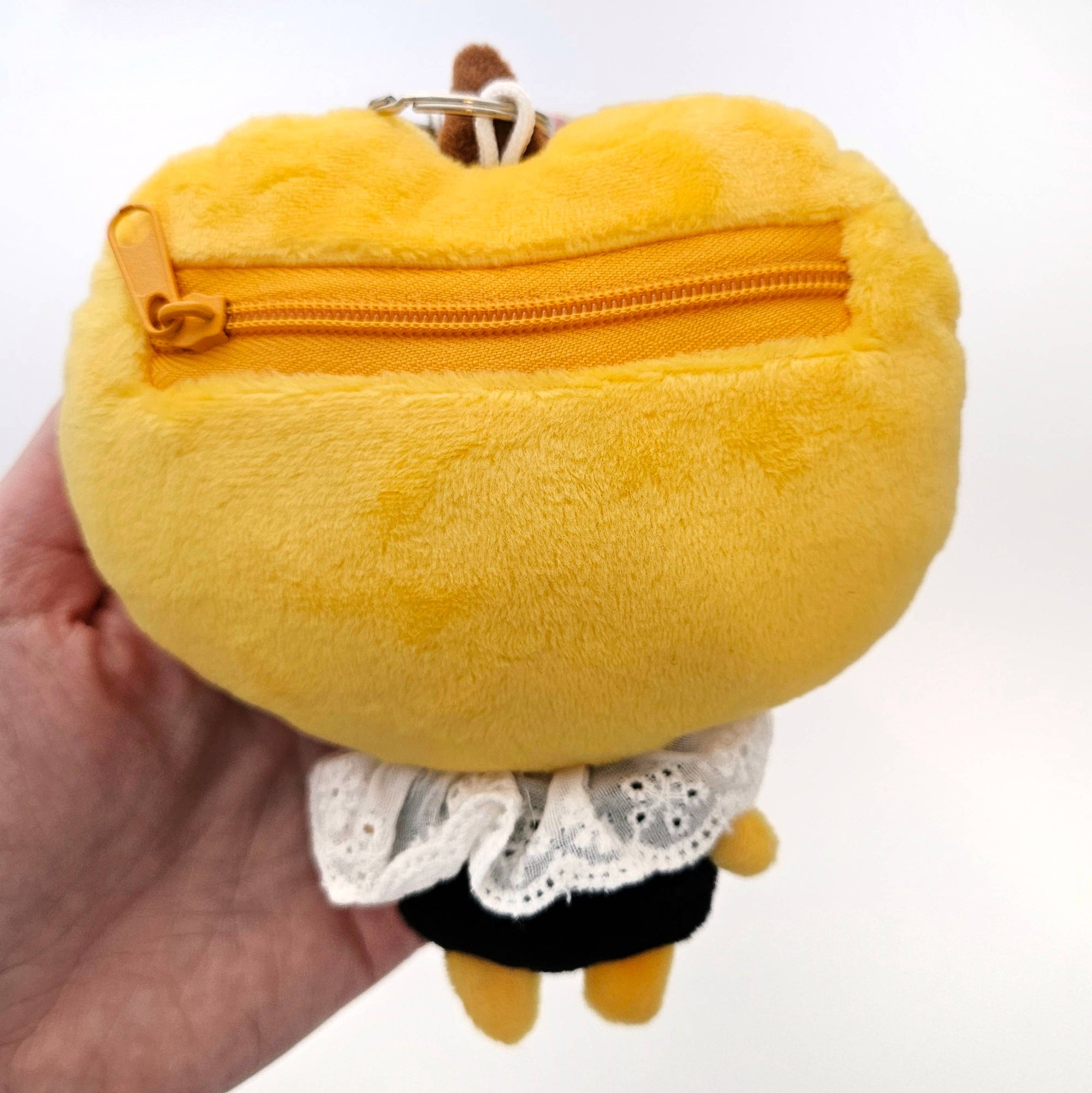 Yellow plush toy with a zipper held by a hand on a white background