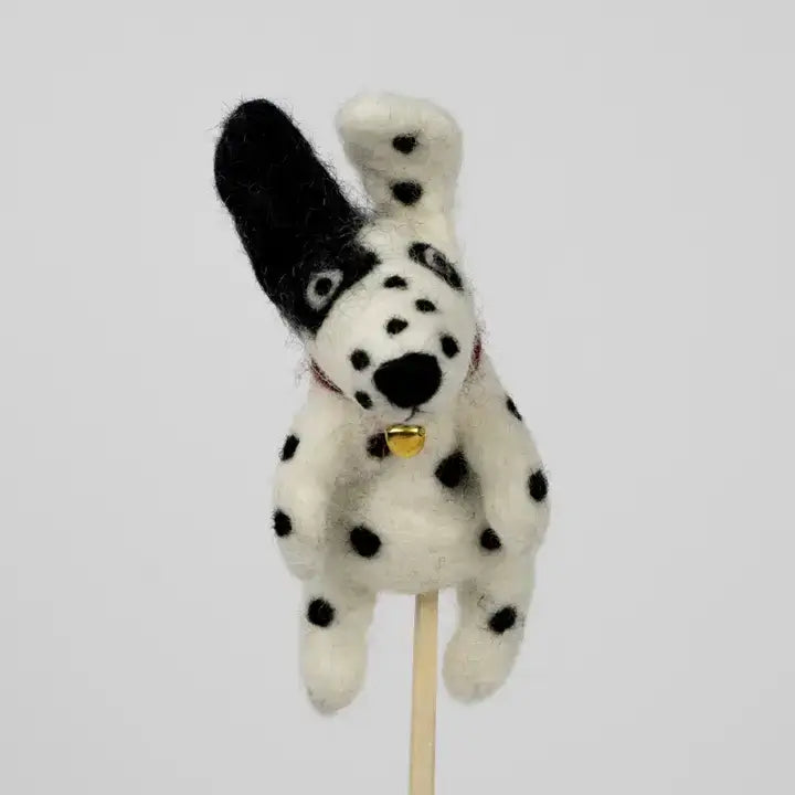 Stuffed toy dog finger puppet with black spots on a stick against a light gray background