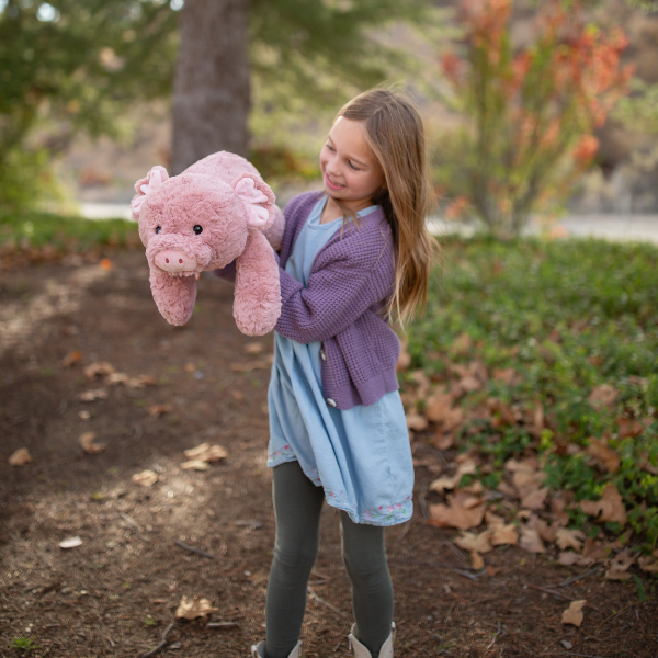 Young girl holding a pink stuffed pig in a park setting