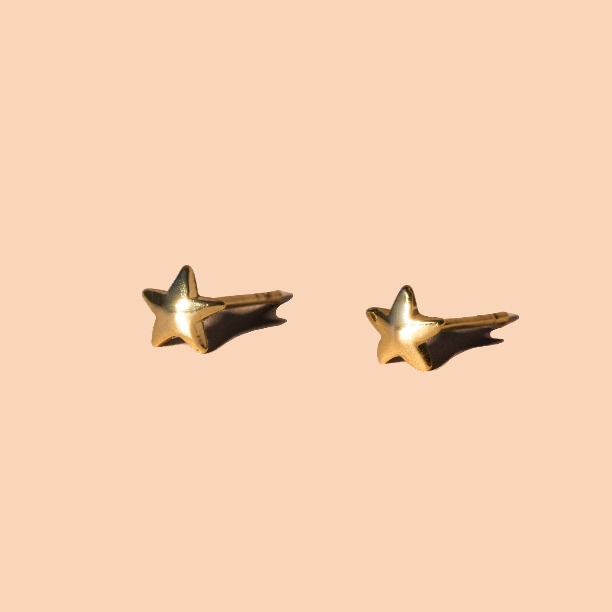 Gold star-shaped earrings on a beige background