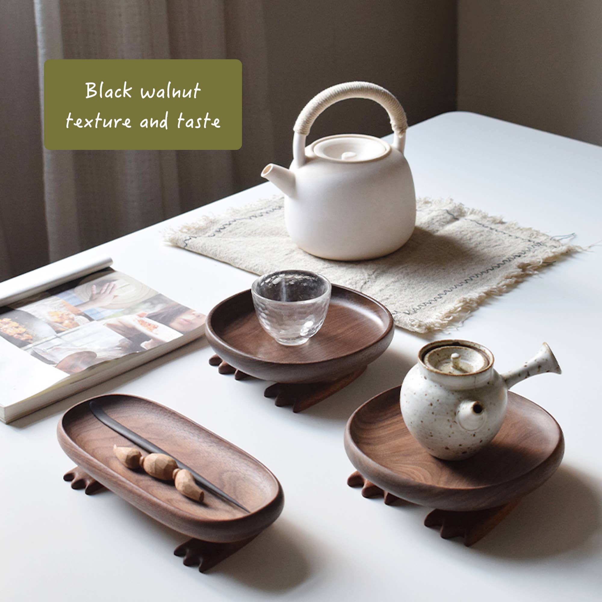 Tea set with white teapot, glass cup, and small ceramic pot on wooden trays on a table.