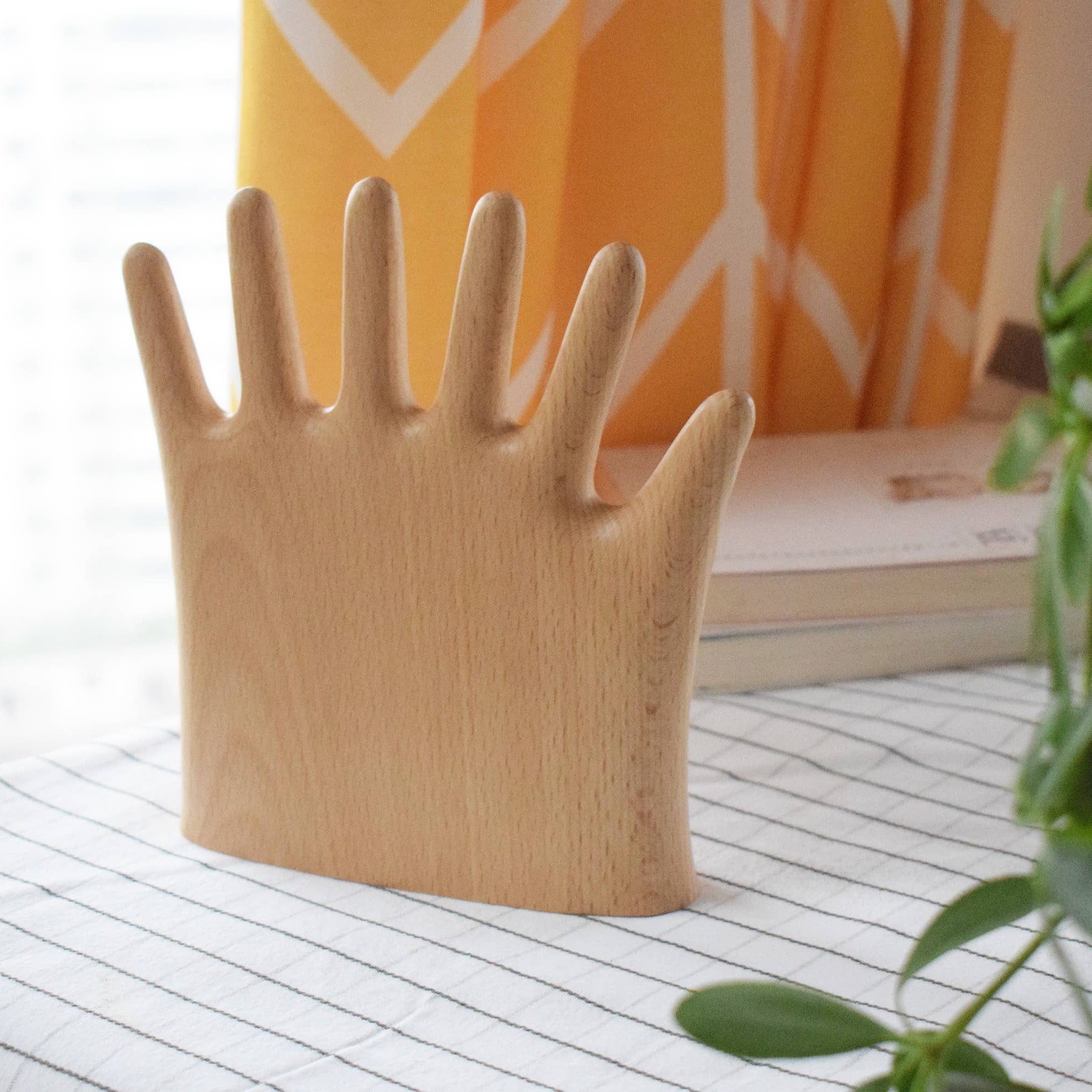 Wooden hand-shaped object on a surface with a plant and books in the background