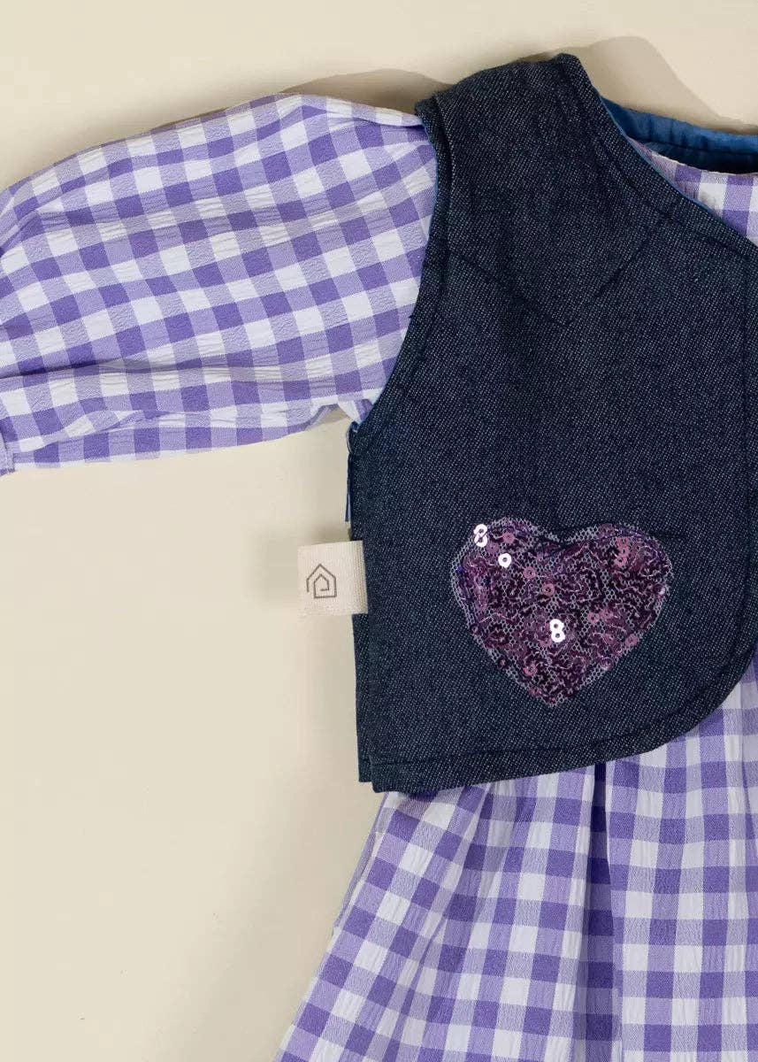 Children's outfit with a purple checkered shirt and dark blue vest with a heart design on a beige background