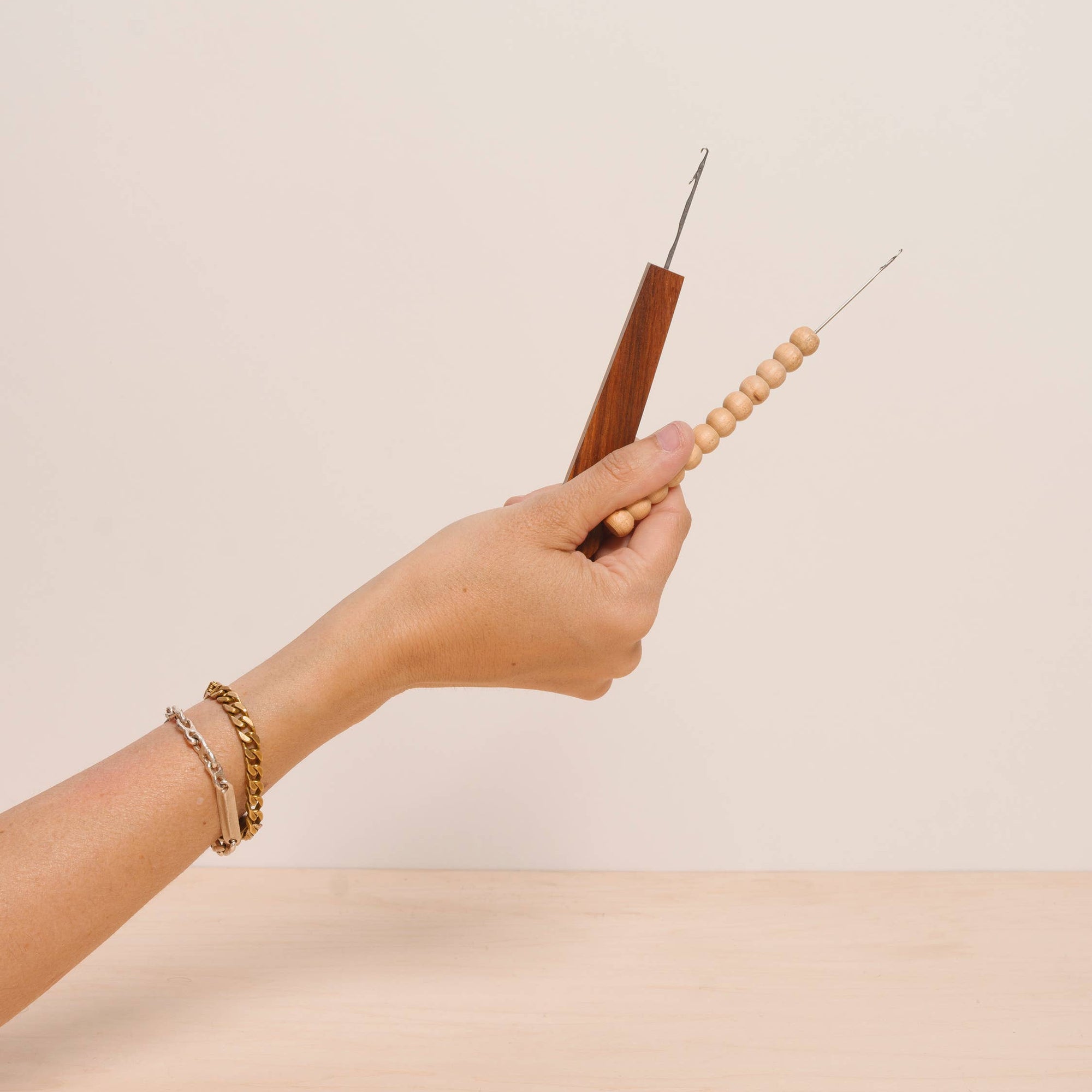 Hand holding a wooden tool with a needle on a beige background