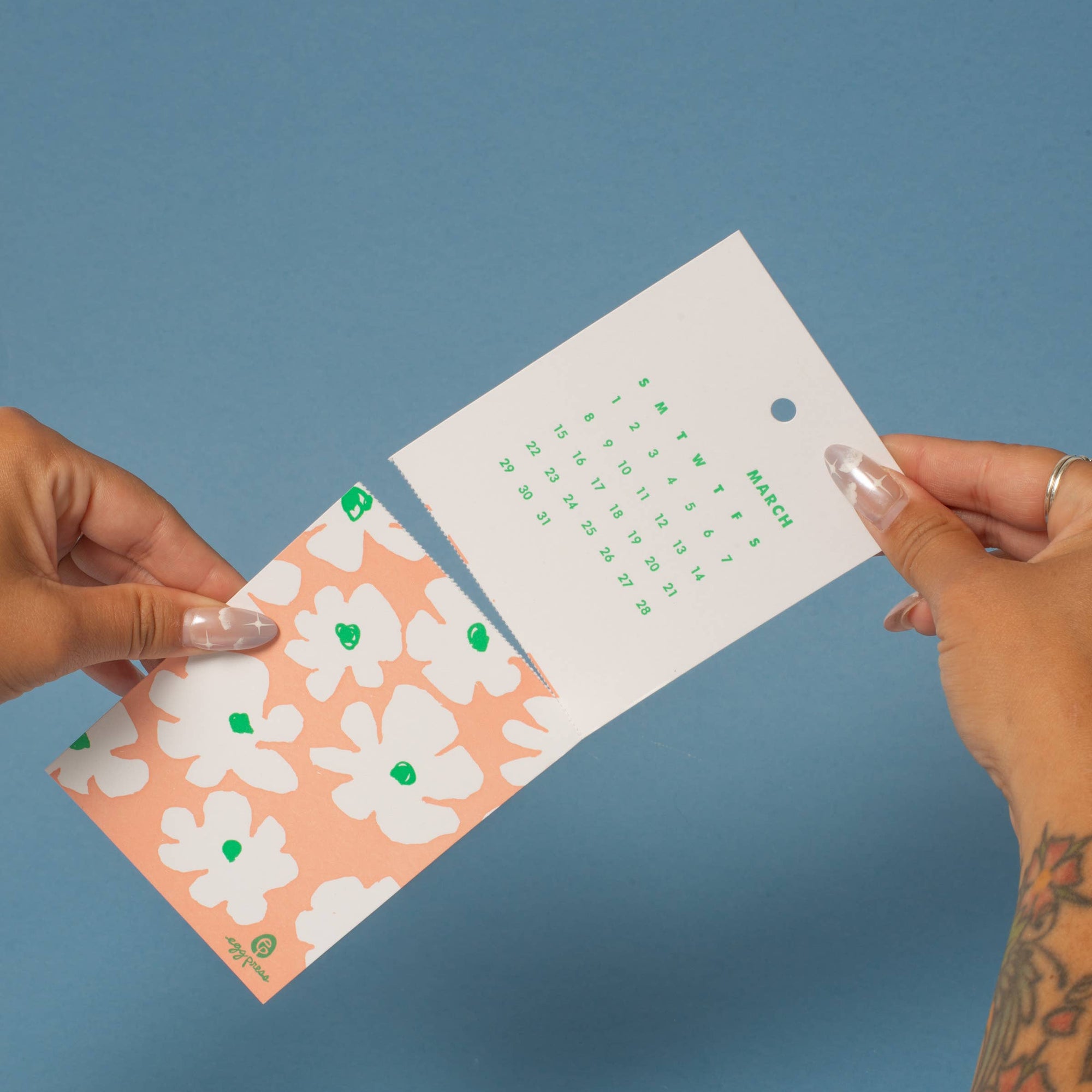 Two hands holding a floral card calendar against a blue background