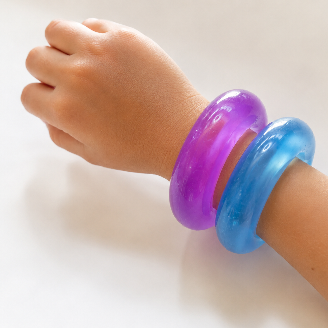 Child's arm wearing a purple and blue bangle on a white background
